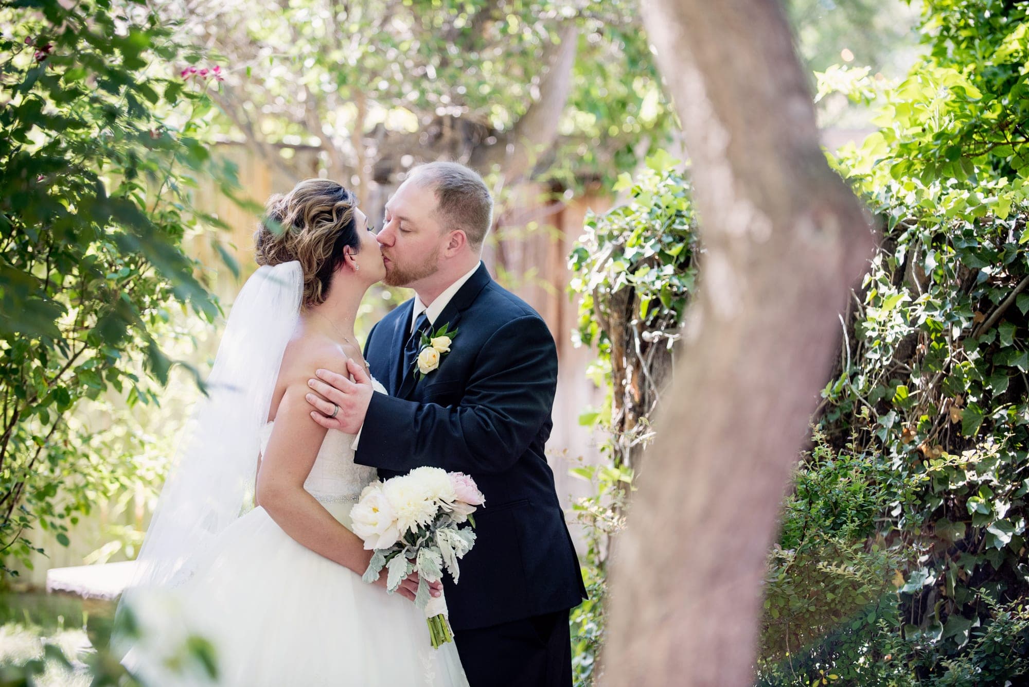 Bride and groom kissing in a lush garden.