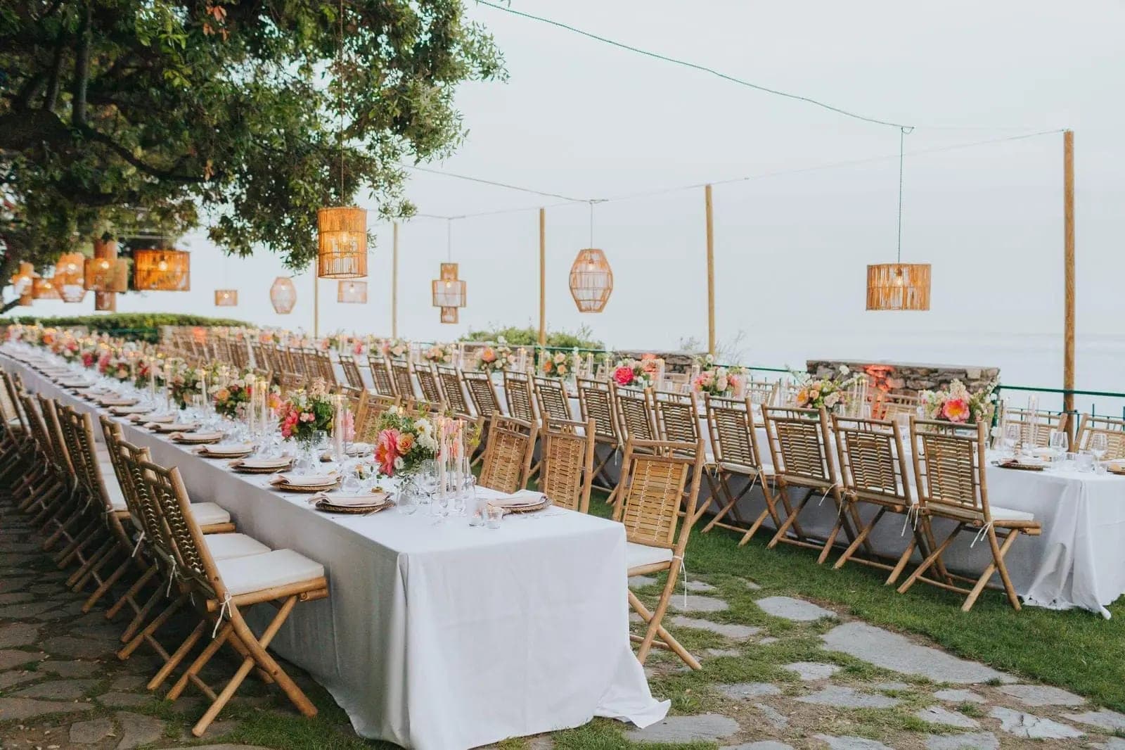 Outdoor reception table setting with chairs and floral arrangements.