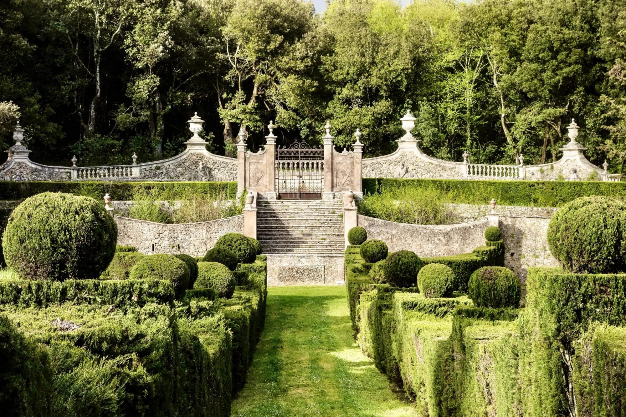 Formal garden with hedges, topiaries, and a stone staircase with a gate.