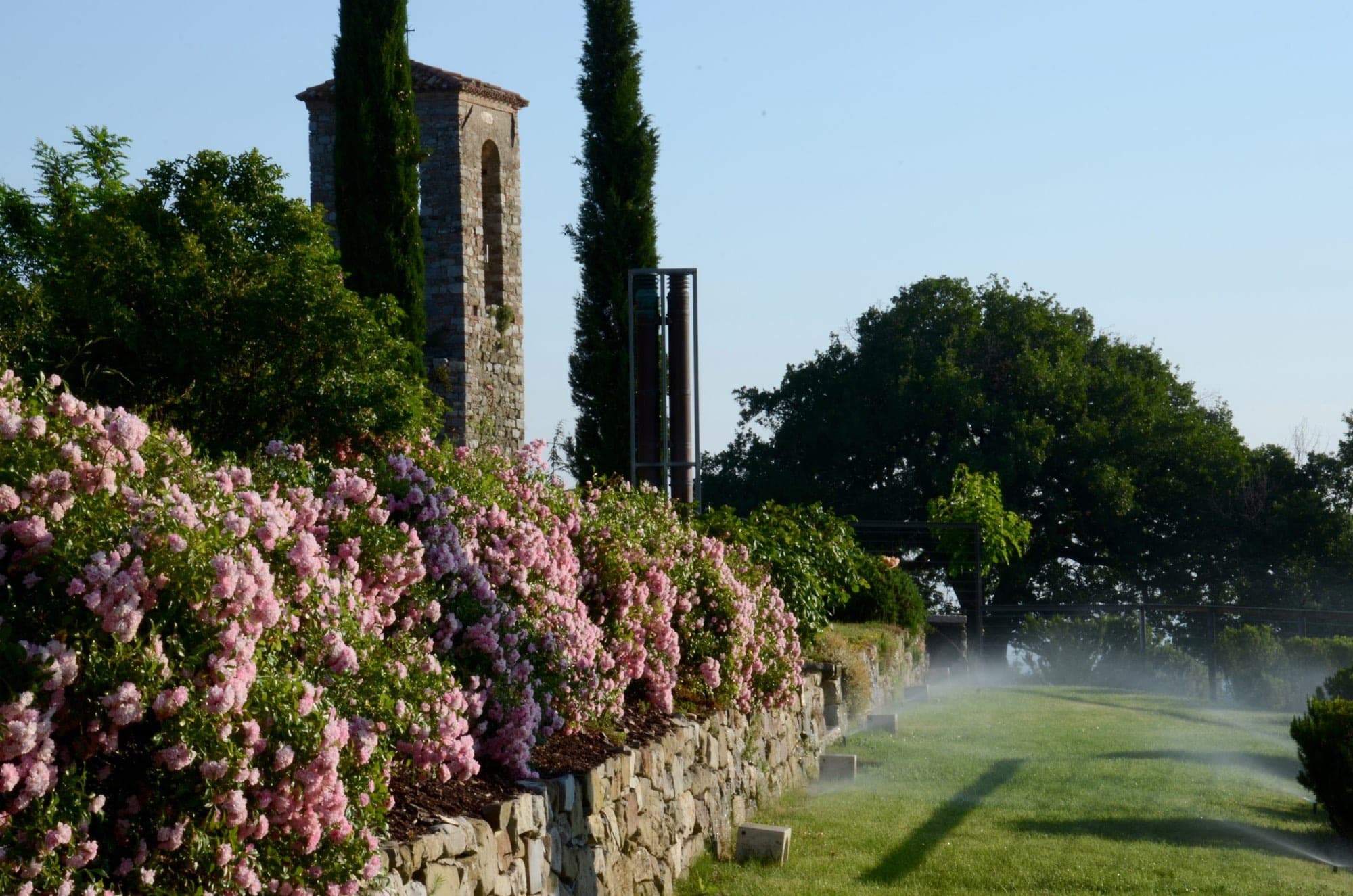 Stone tower and rose bushes beside a misted lawn at a venue.