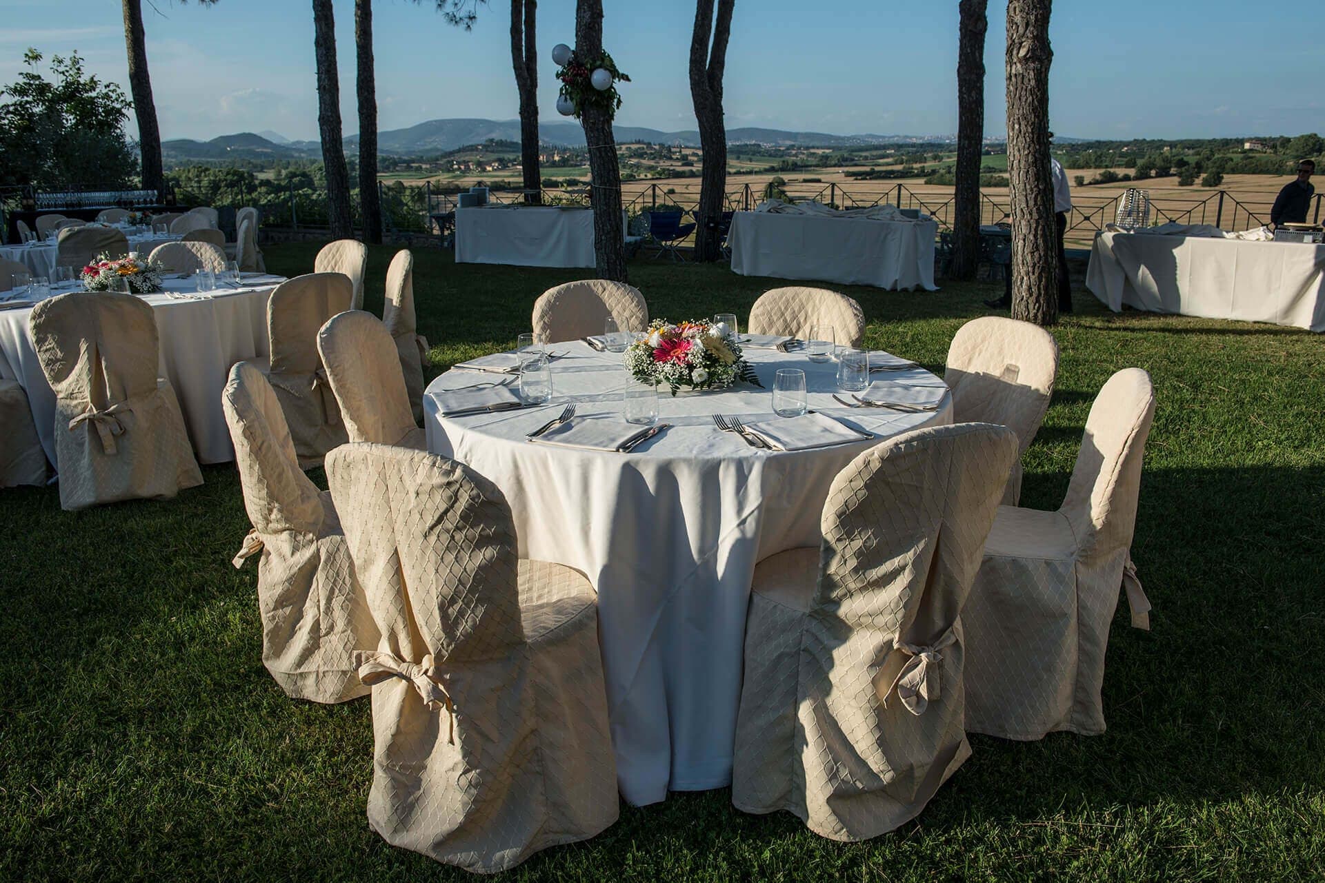 Outdoor reception tables set with white tablecloths and chairs on a lawn with a view of rolling hills.