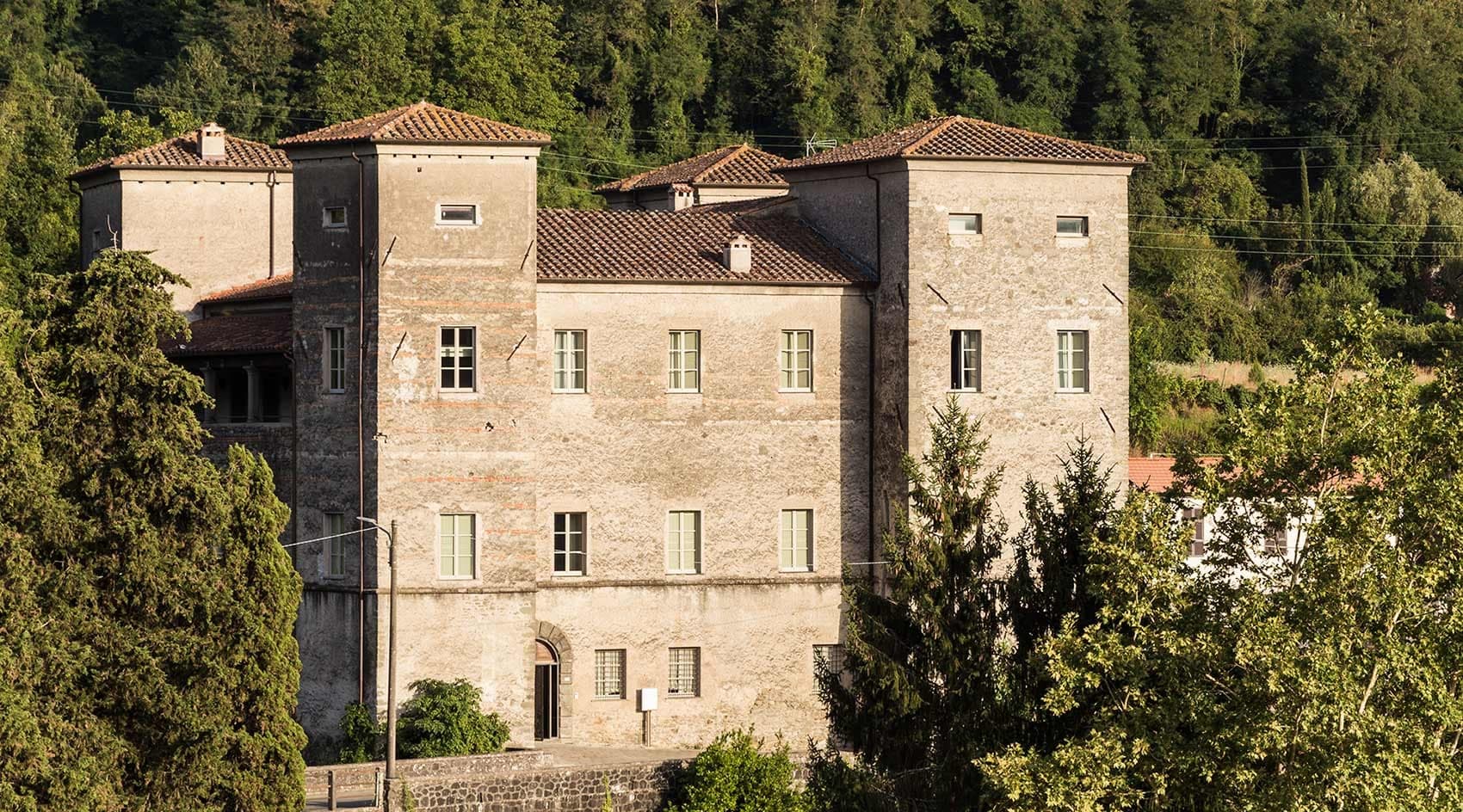 The stone exterior of a historic building with towers, surrounded by trees.