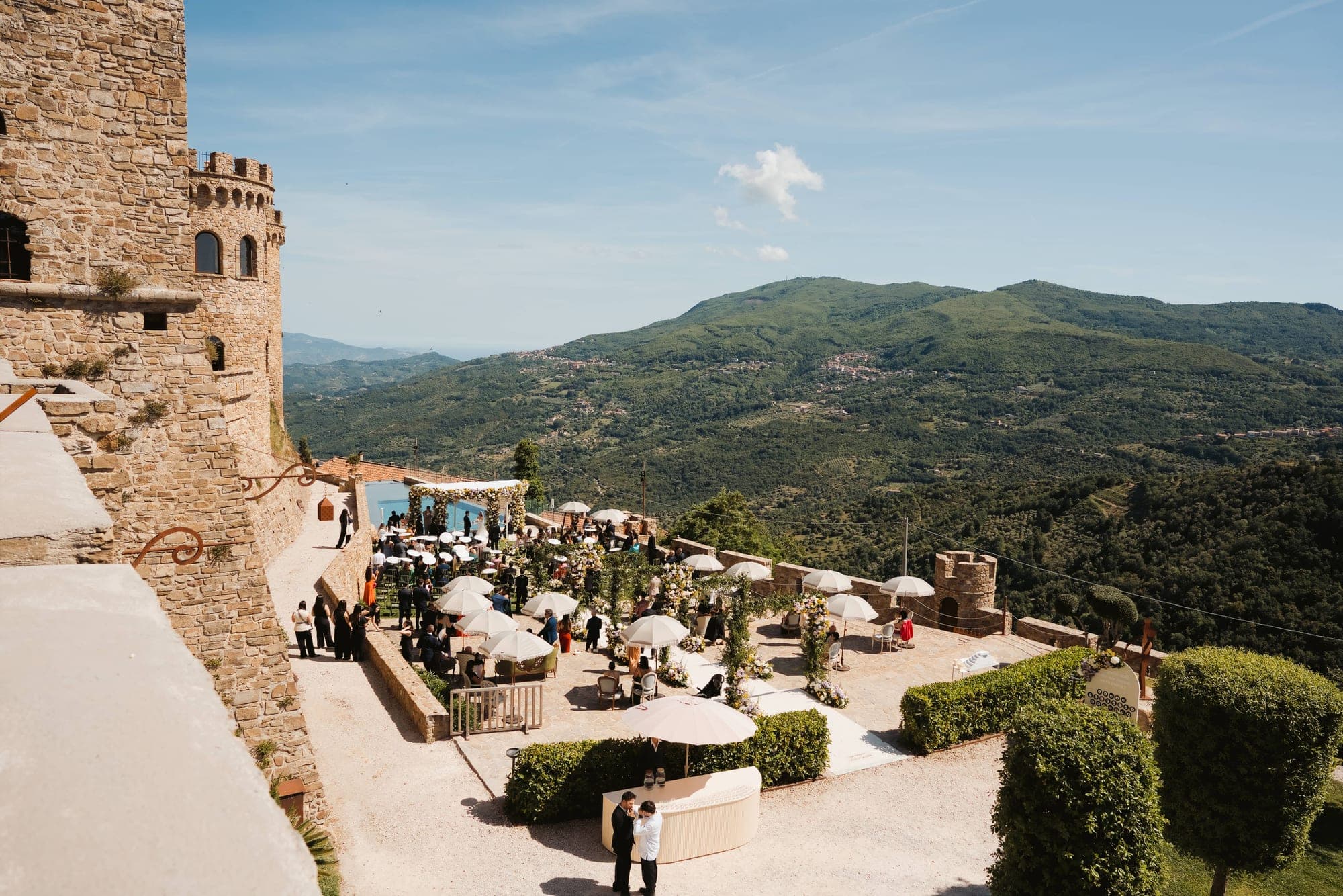 Wedding ceremony on a terrace with a castle and hills in the background.