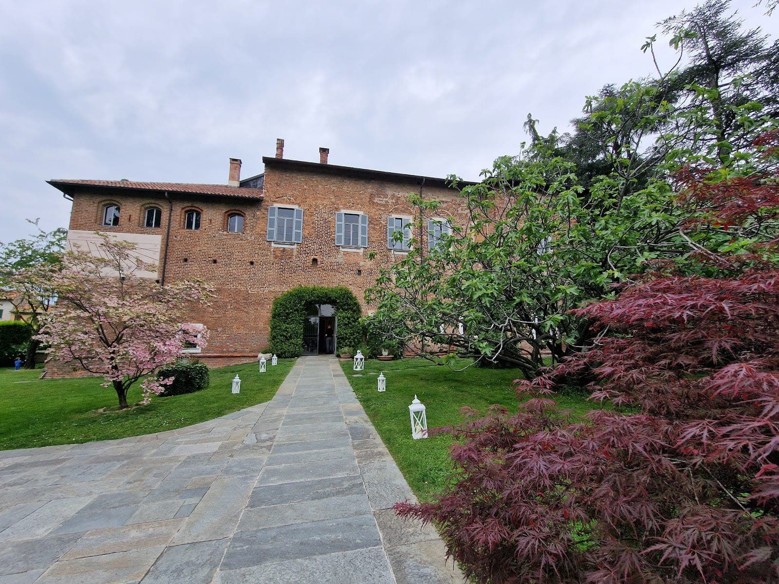 A stone pathway leads to the entrance of a brick building surrounded by greenery and trees.