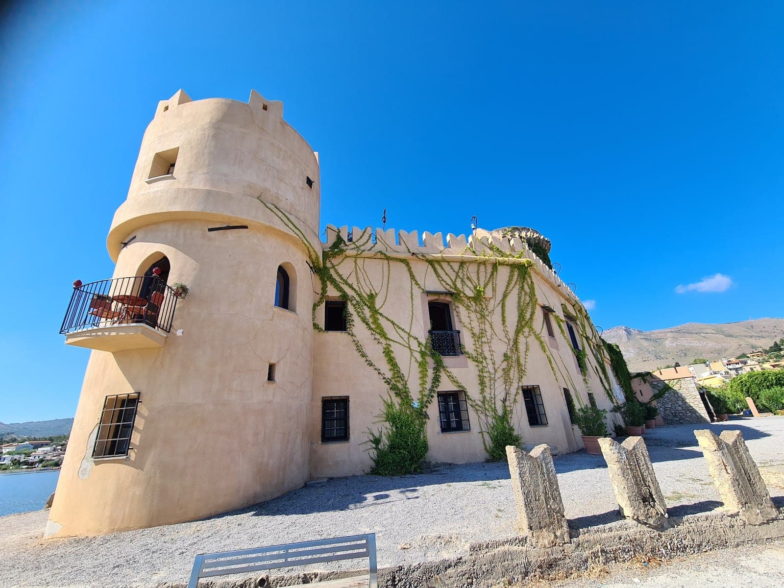 Exterior of a castle with a tower and ivy-covered walls under a blue sky.