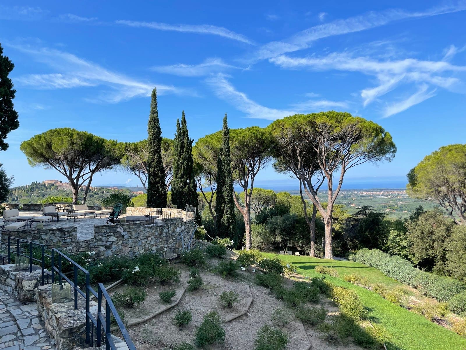 Terrace and gardens with pine trees overlooking the sea and a distant town.