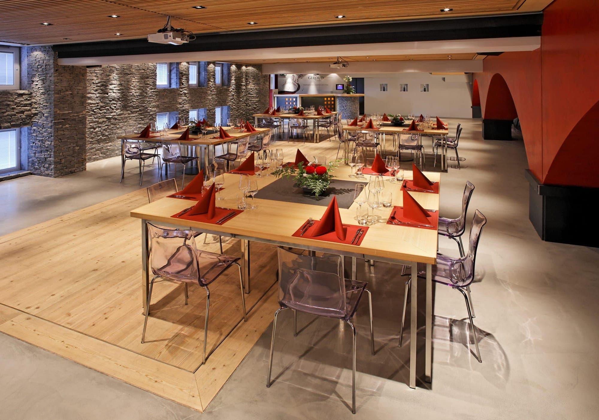 A reception room with tables set for a wedding and transparent chairs.