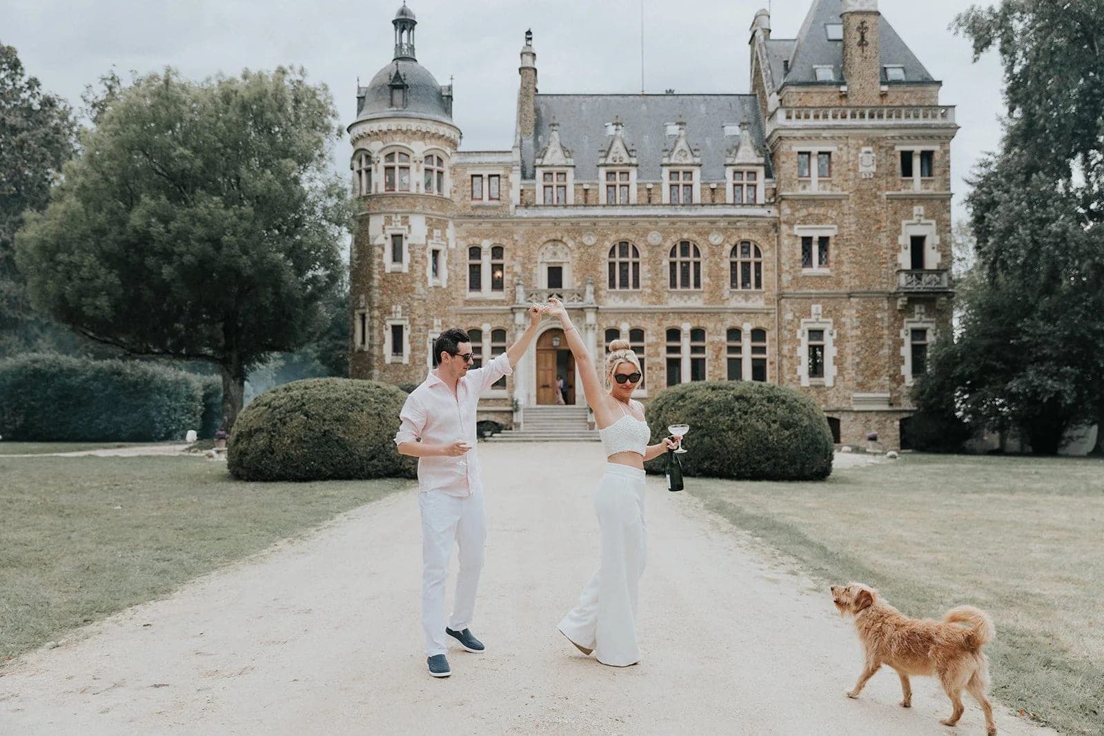 A couple dances on the grounds of a castle with a dog nearby.