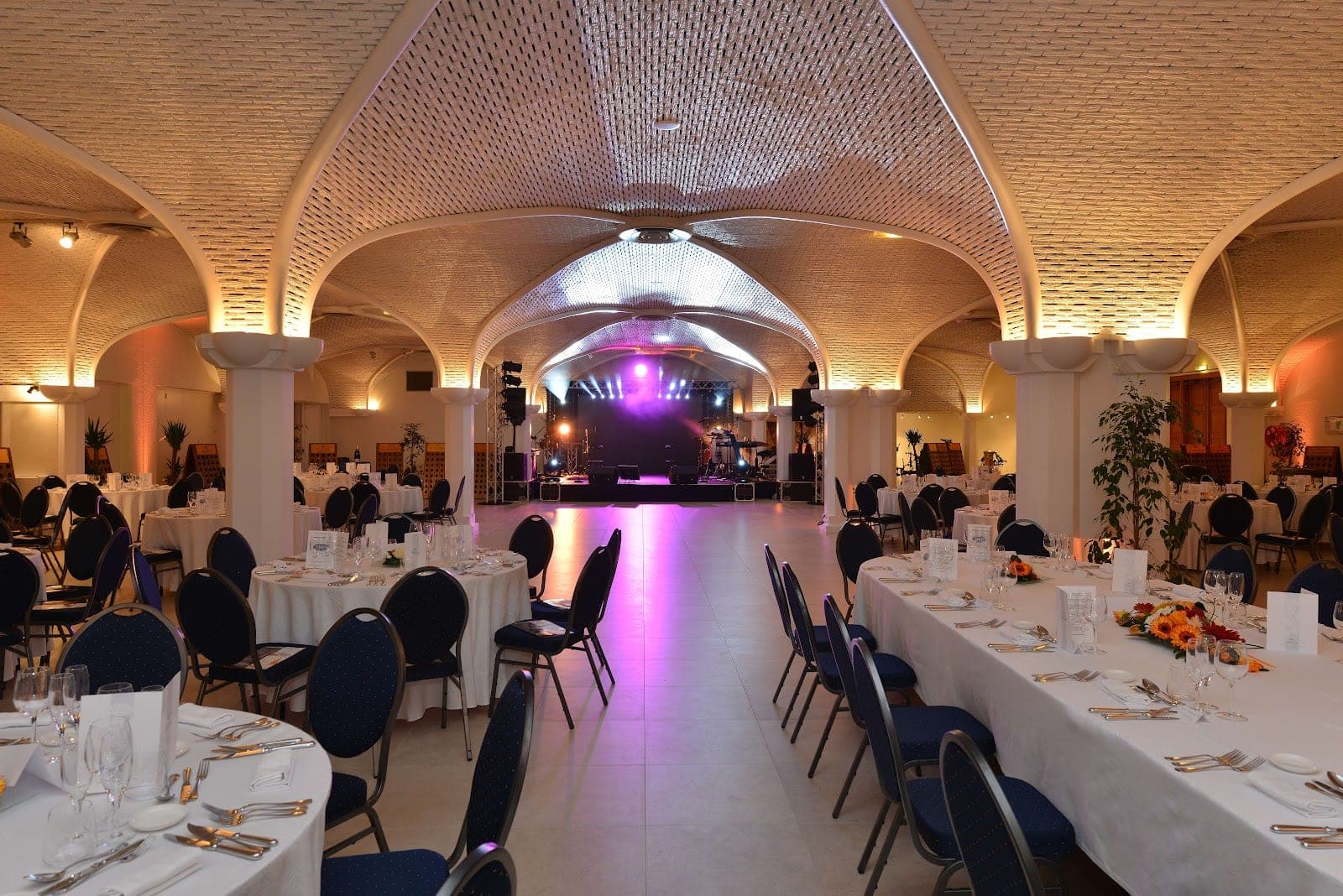 A reception hall with arched ceilings, set tables, and a stage with lighting.