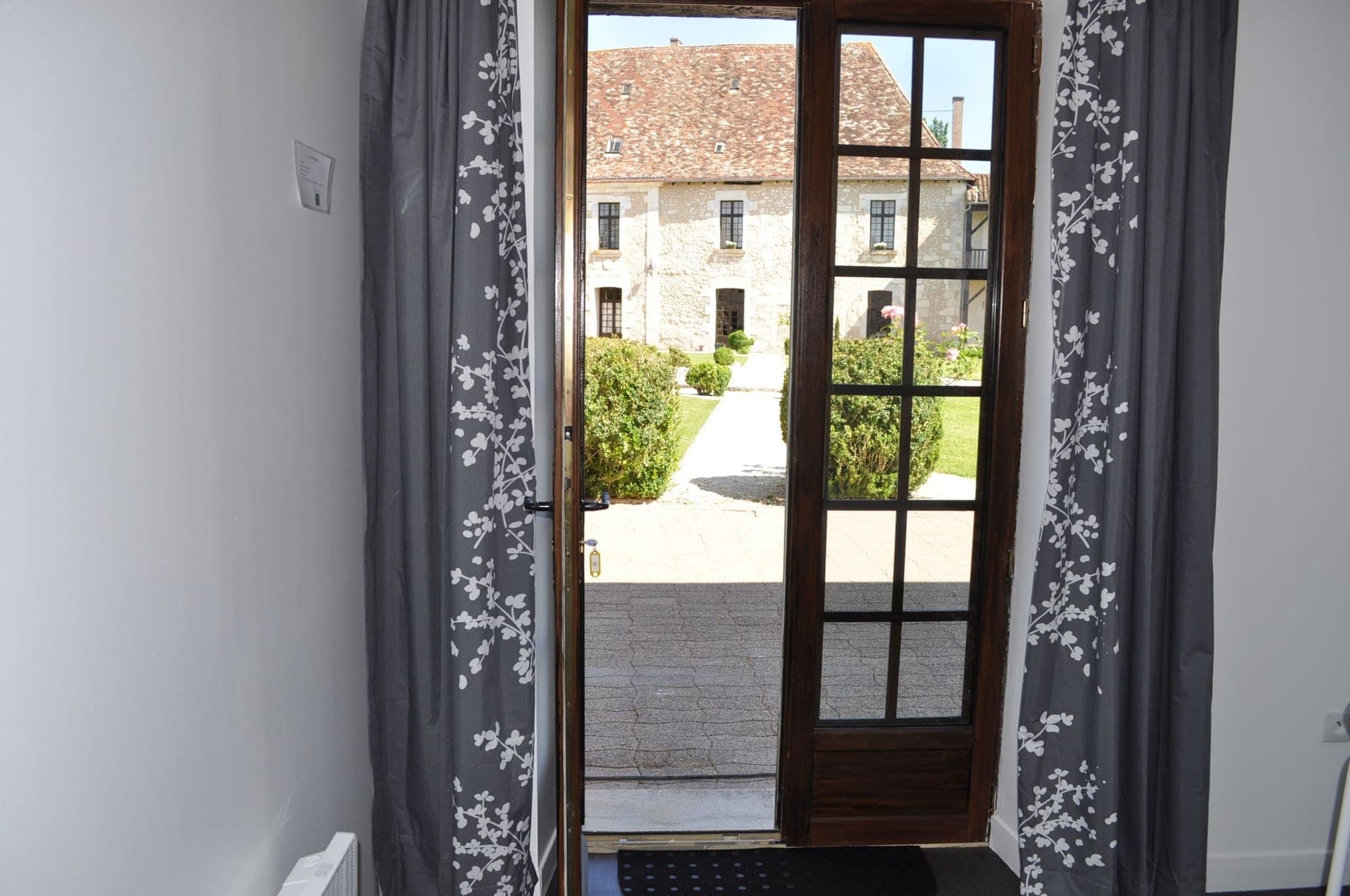 View of a stone building with a tiled roof through a doorway with curtains.