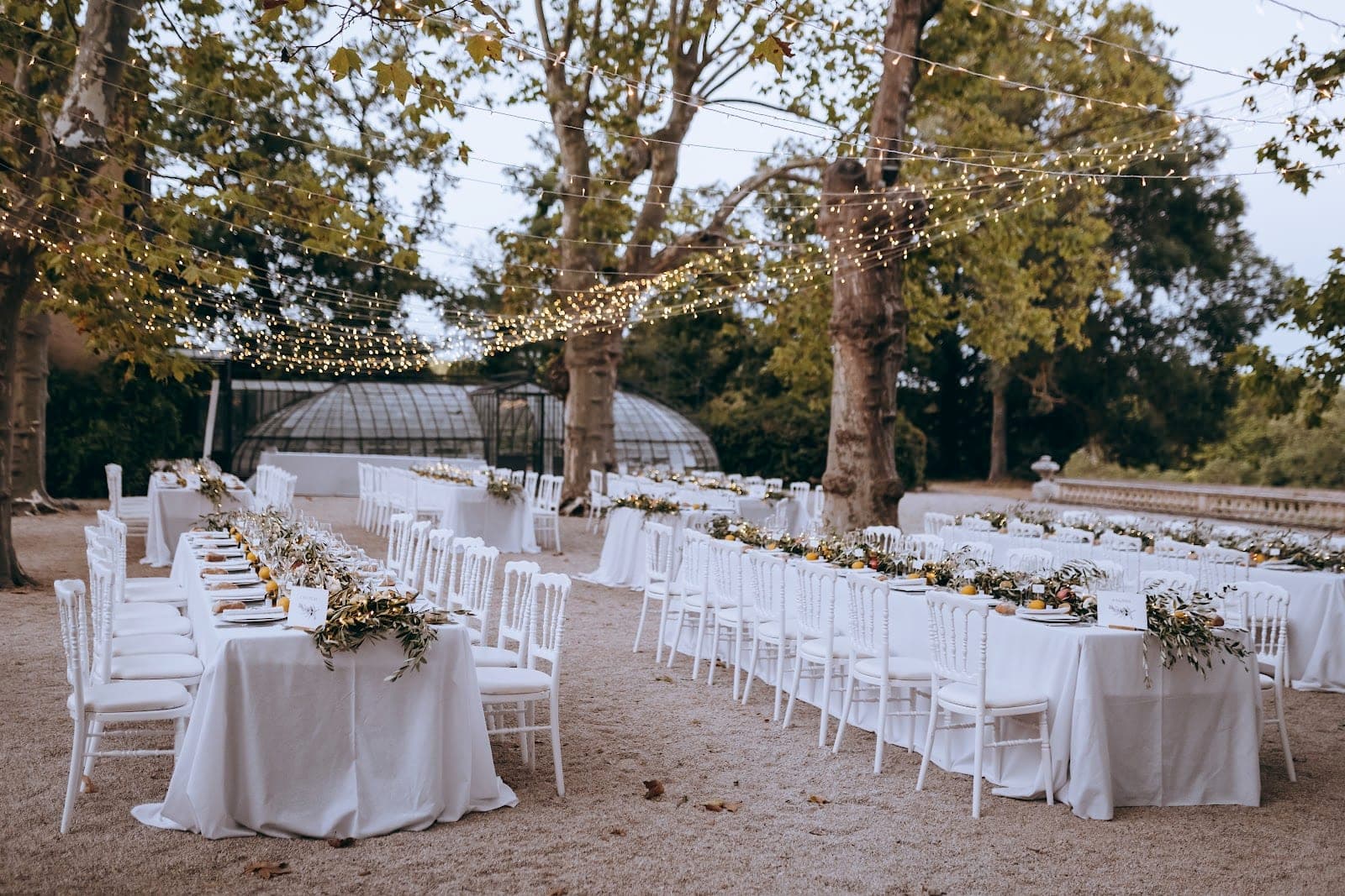 Outdoor reception tables and chairs set up under trees with string lights.