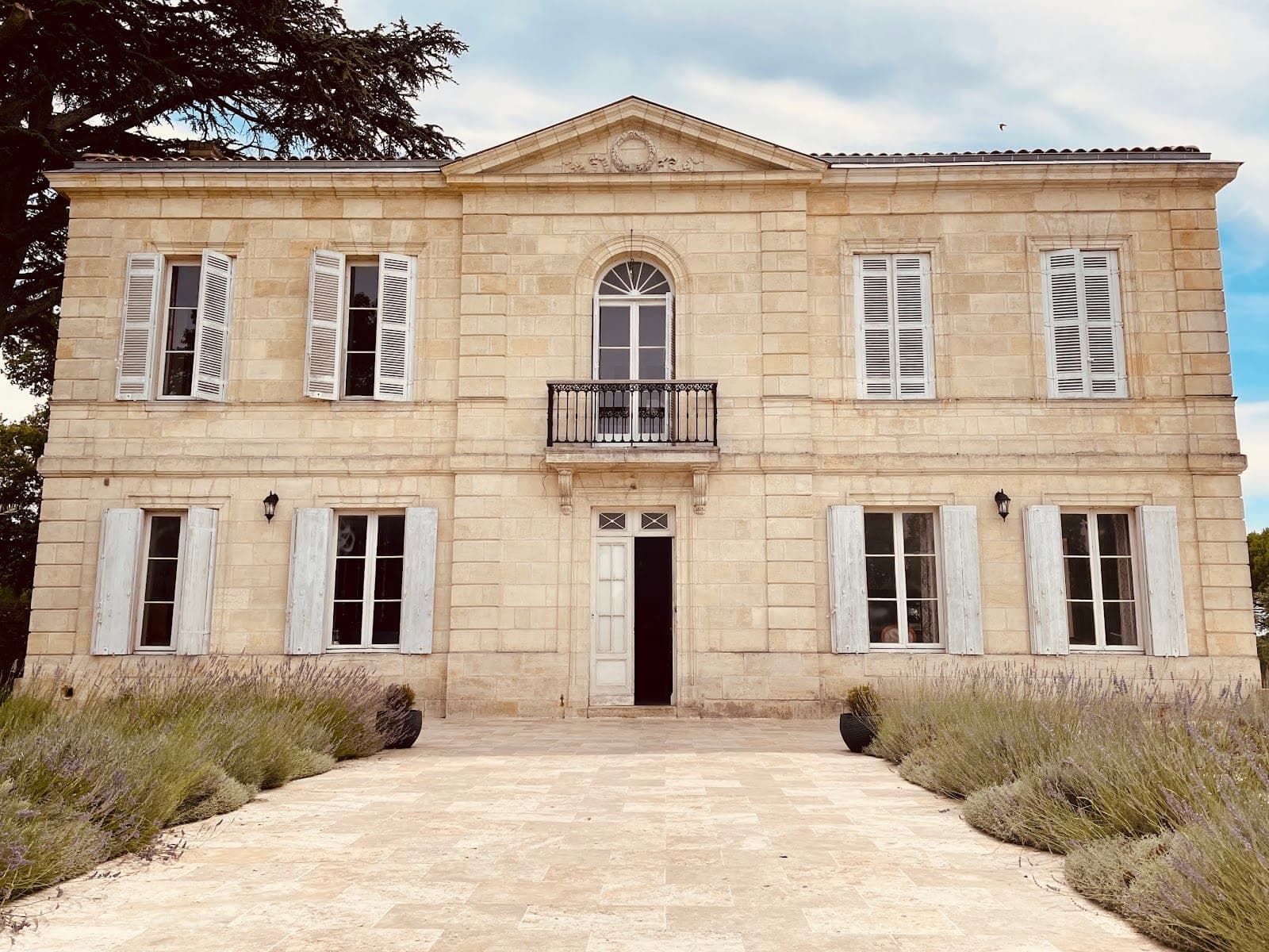 Exterior of a stone chateau with white shutters and lavender bushes.