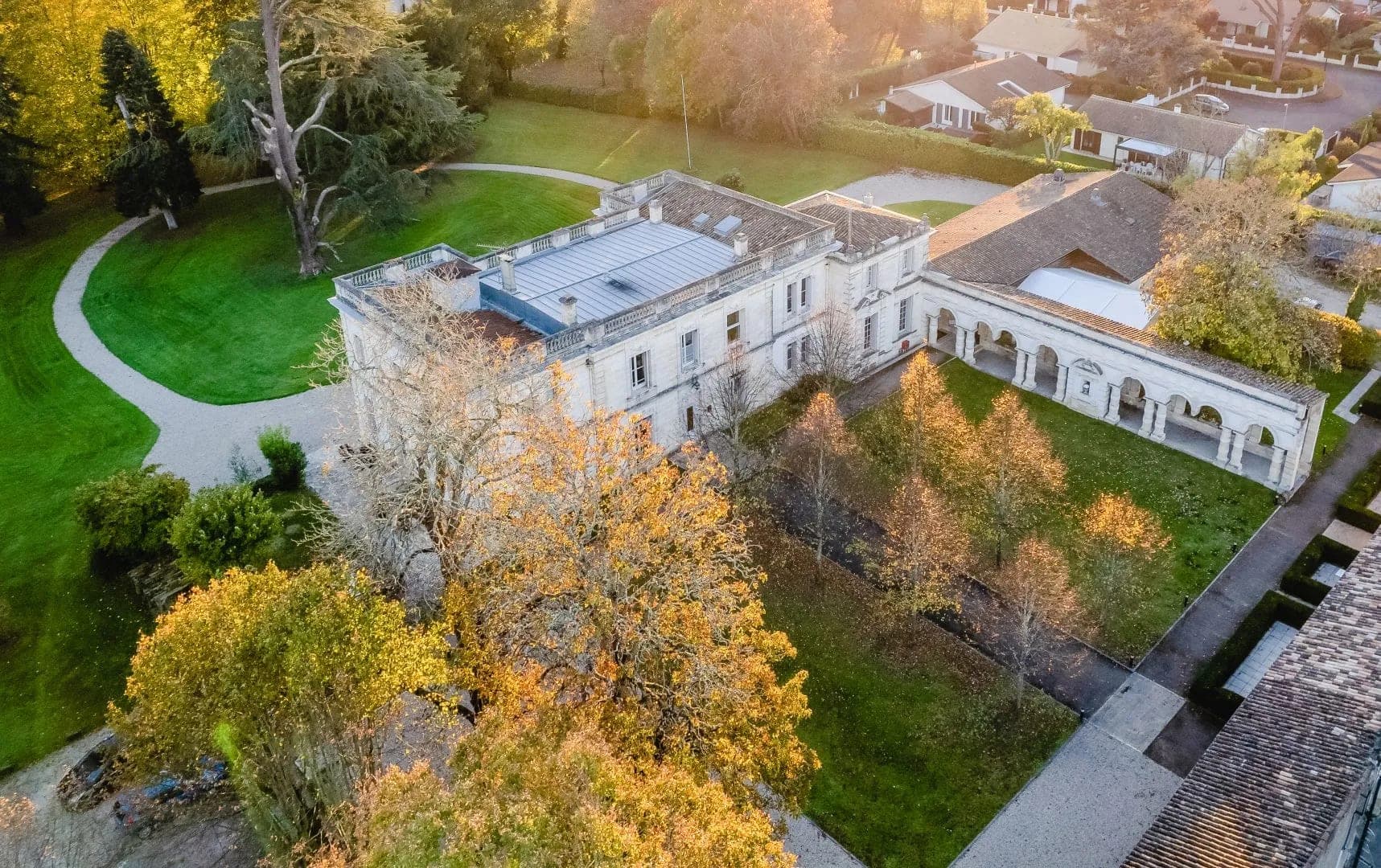 Aerial view of a chateau with surrounding gardens and trees in autumn.