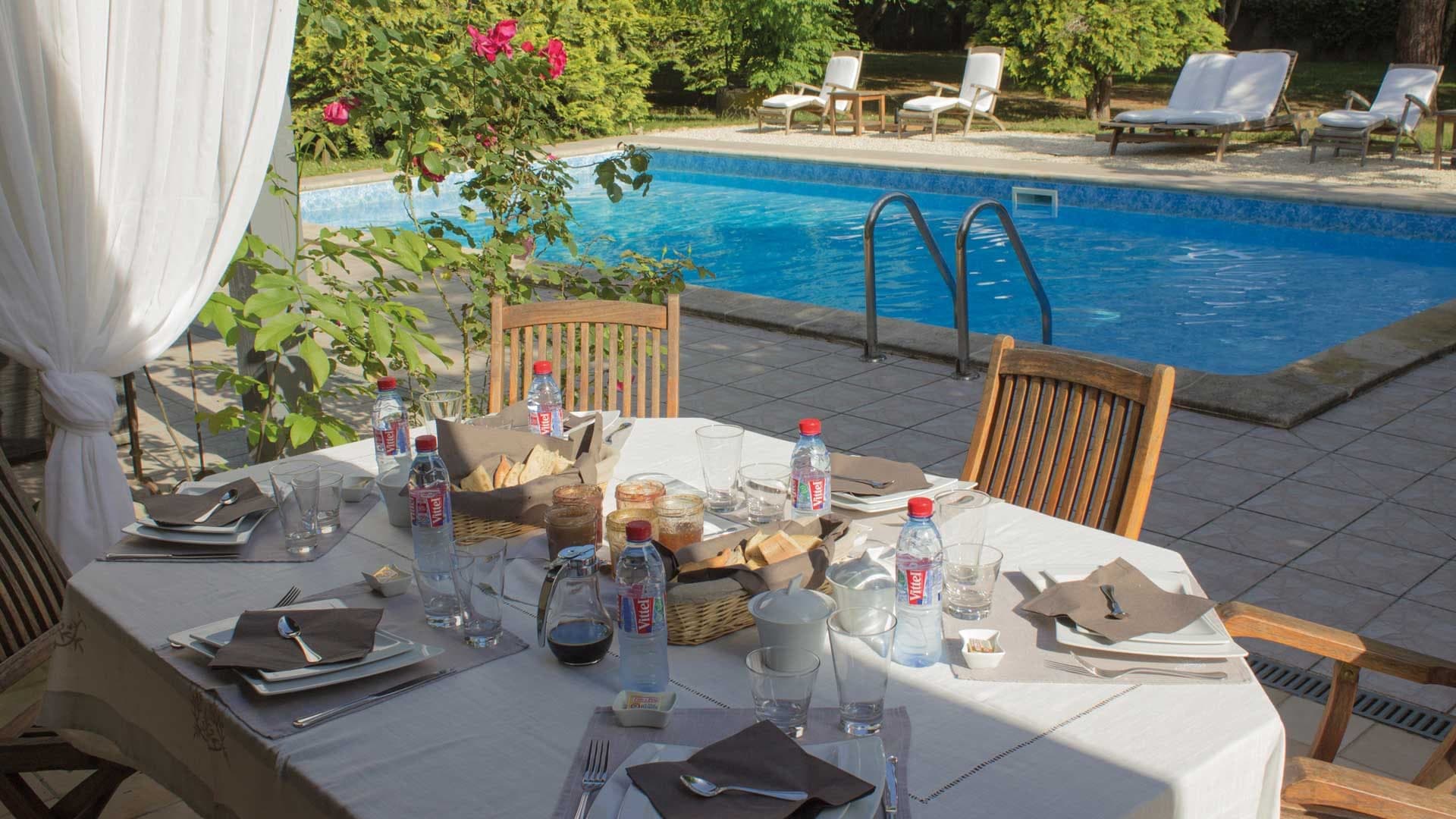 Table set for a meal by a swimming pool with lounge chairs in the background.