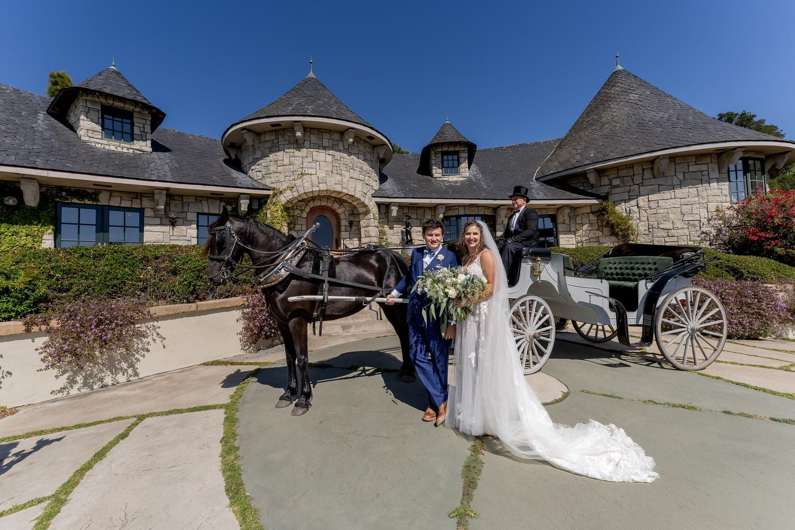 Wedding couple with horse-drawn carriage in front of a stone building.