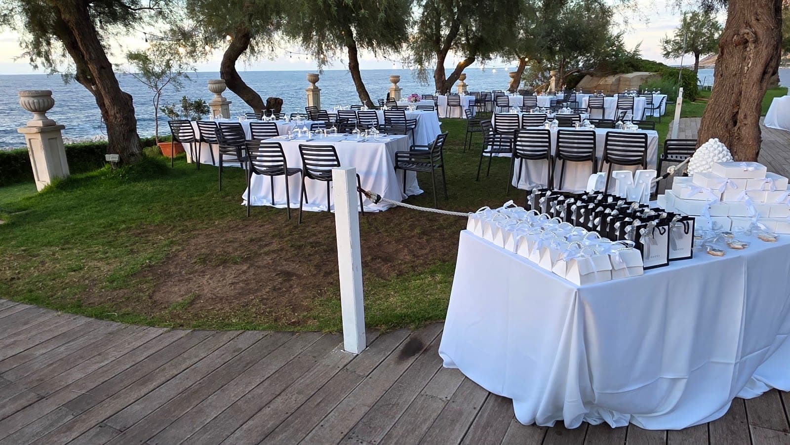 Outdoor wedding reception tables set up by the sea with gift bags on a table.