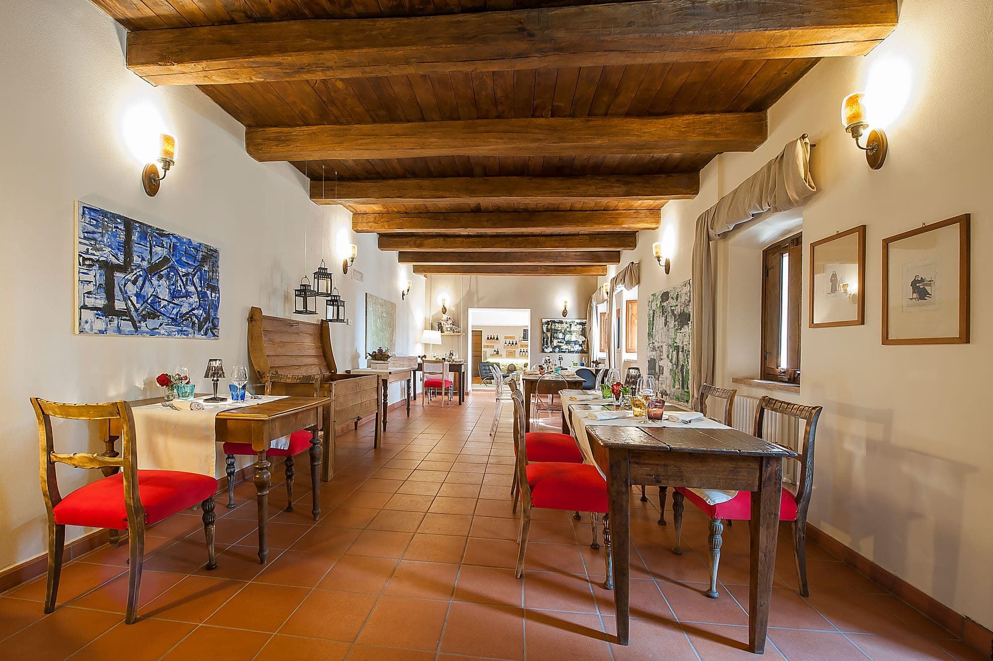 Dining room with wooden beams, terracotta floors, and tables set for a meal.