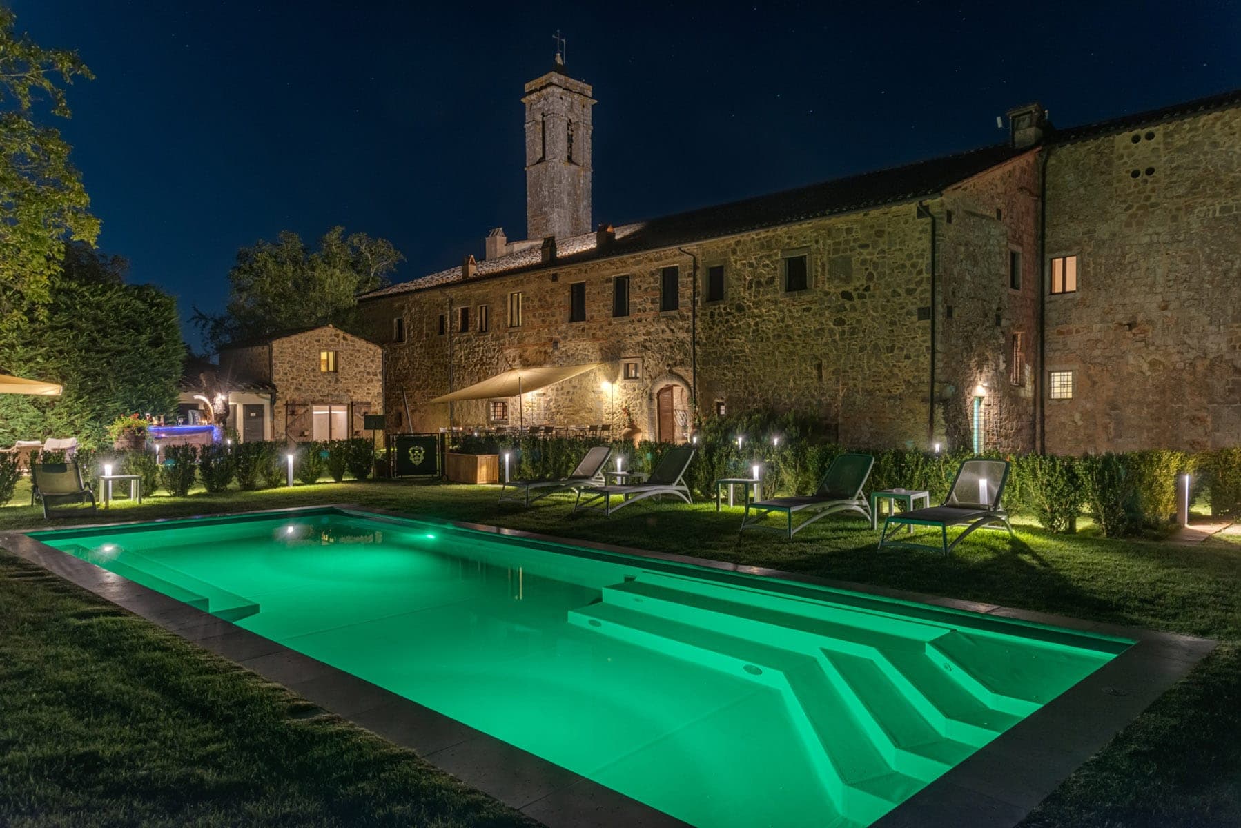 A swimming pool with green lighting in front of a stone building at night.
