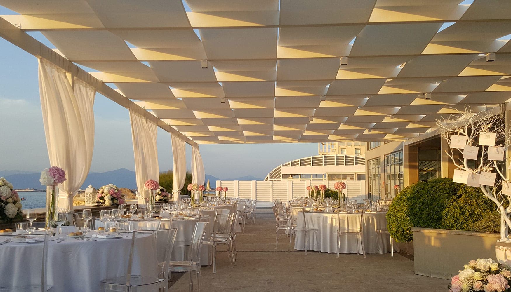 Outdoor reception area with tables set for a wedding, overlooking the sea.