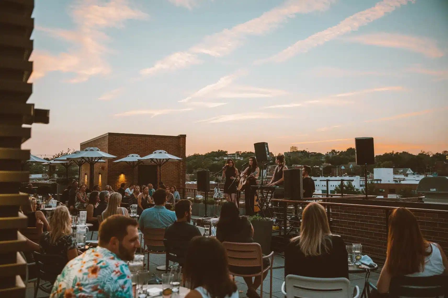 A band plays on a rooftop at sunset with guests seated at tables.
