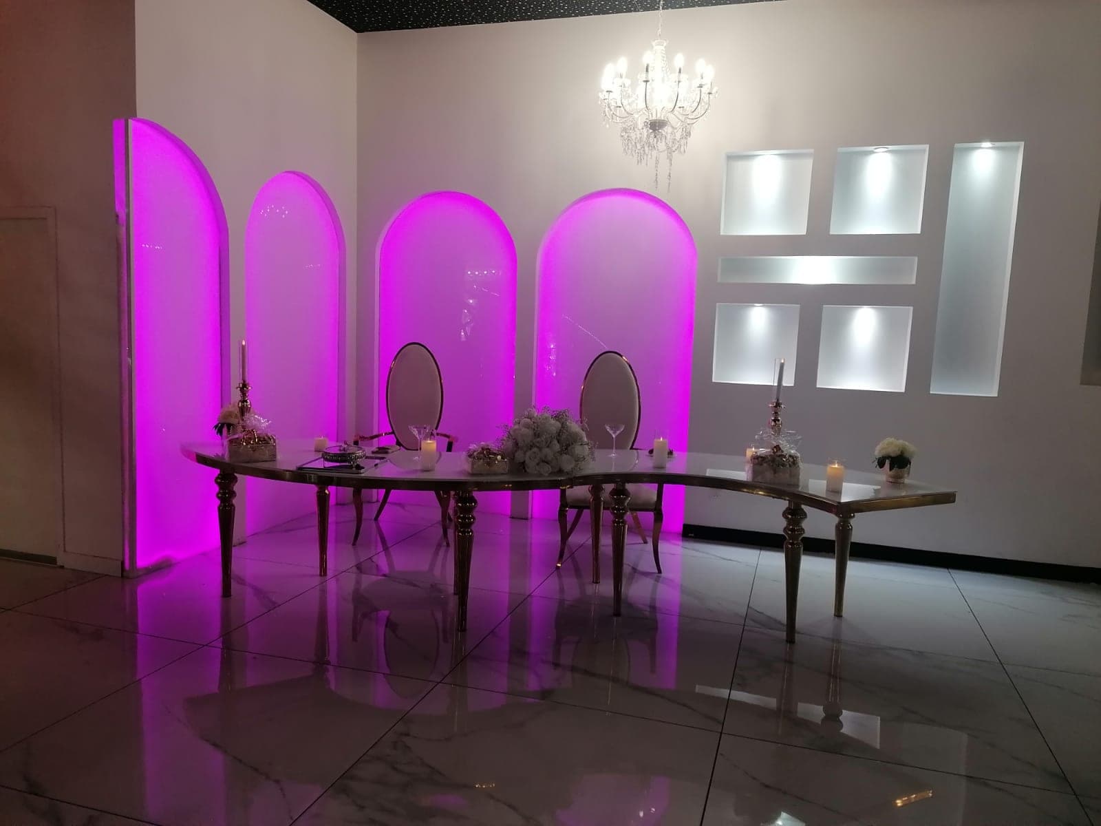 A table set for two with pink arched backdrops and a chandelier.