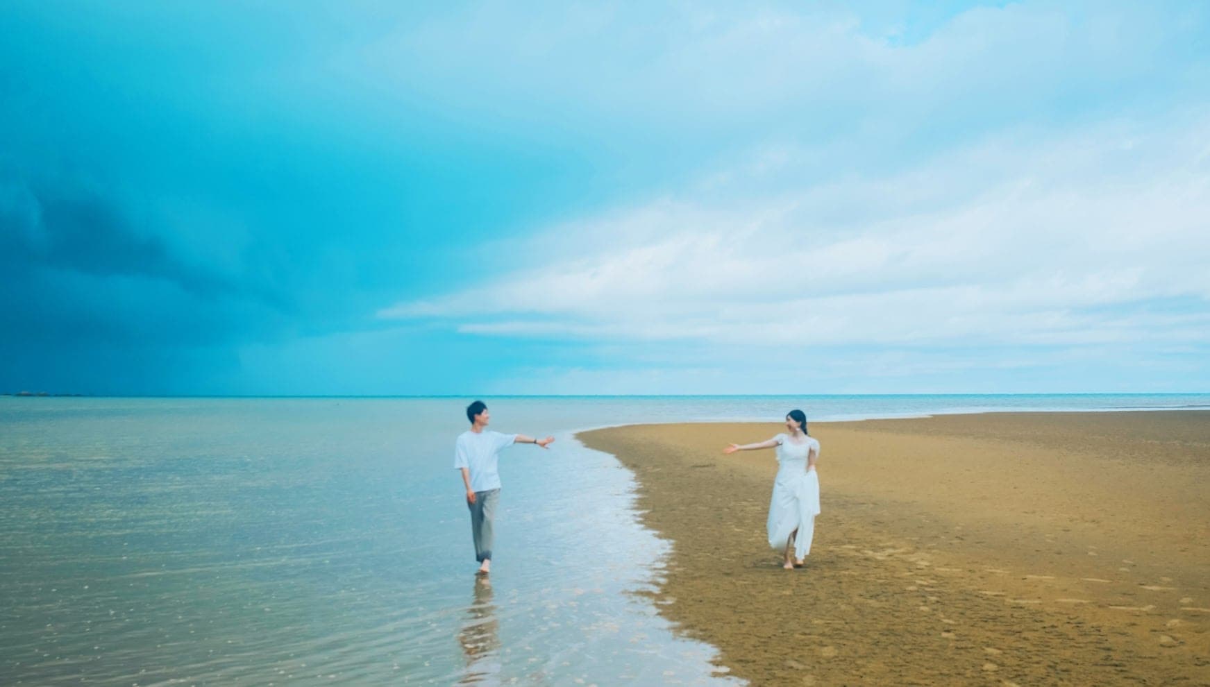 A couple stands on a beach with the ocean and sky in the background.