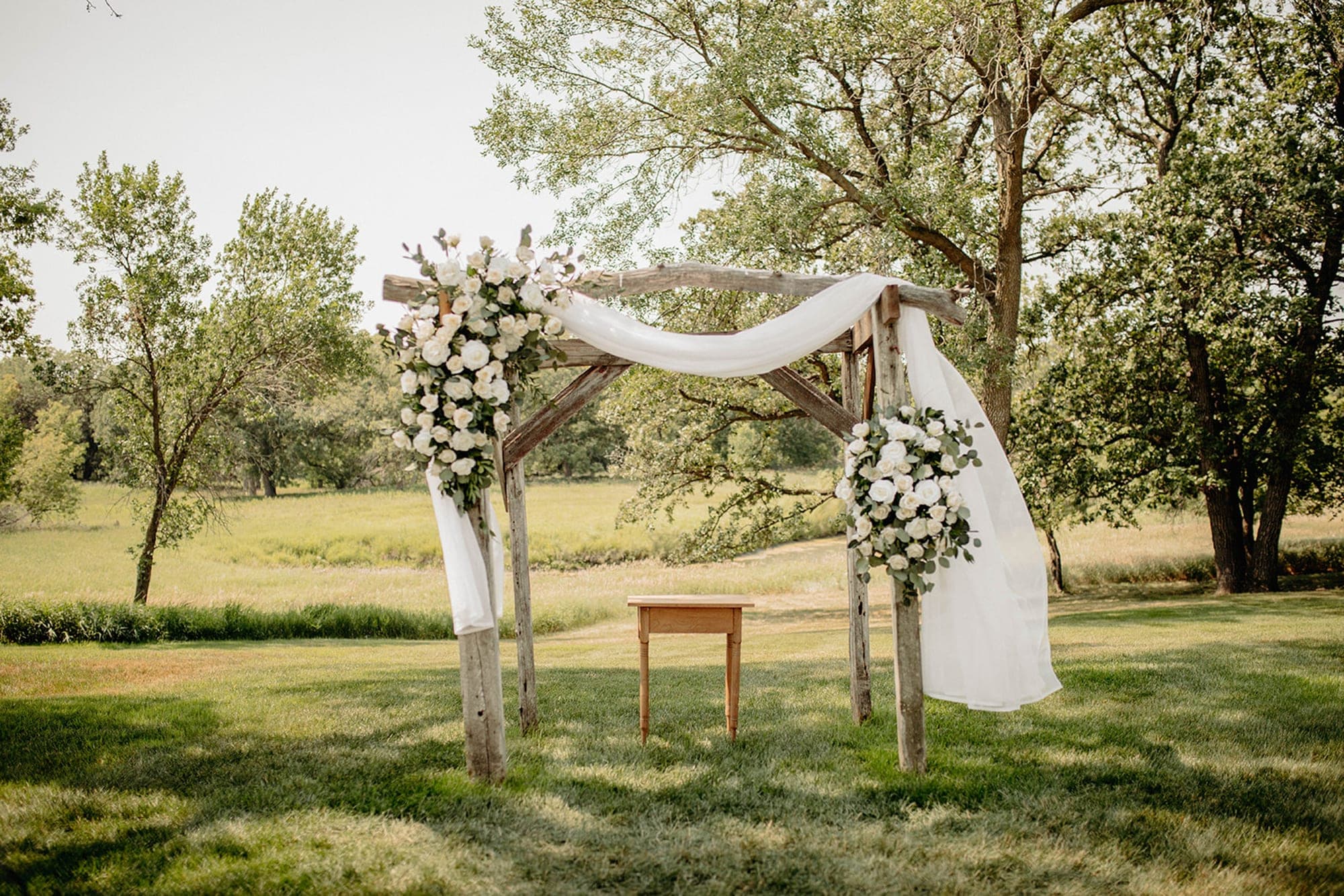 Outdoor wedding arch with flowers and fabric in a grassy field.