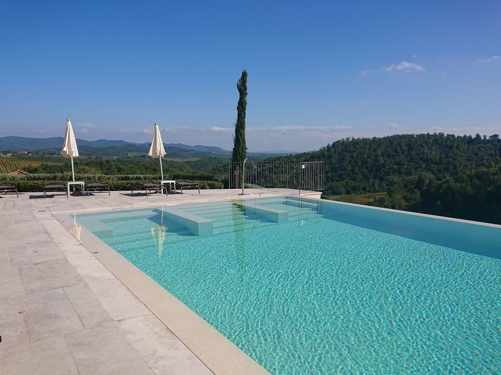 Infinity swimming pool overlooking rolling hills and vineyards under a clear blue sky.