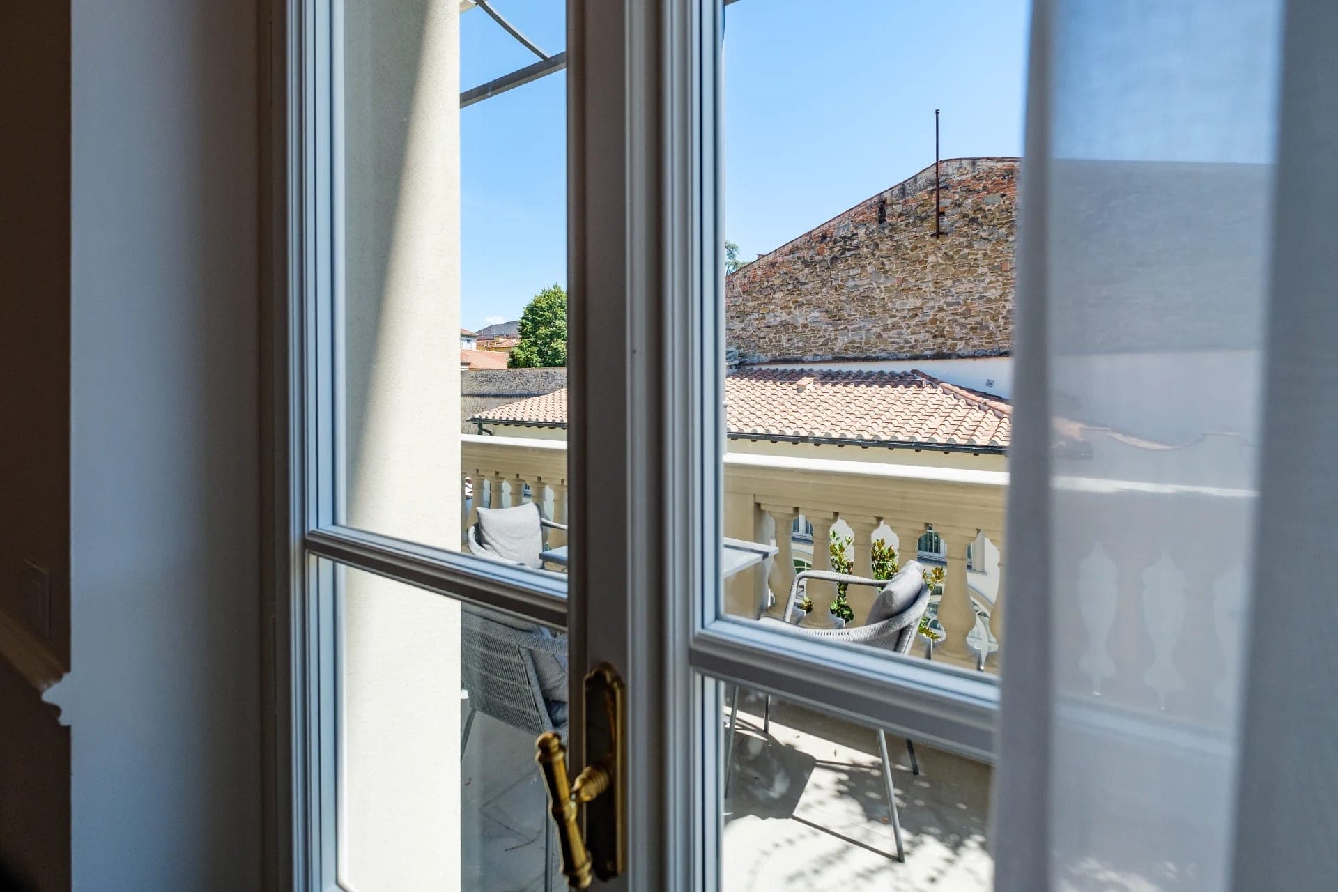 View from a window of a balcony with chairs and a stone wall in the background.