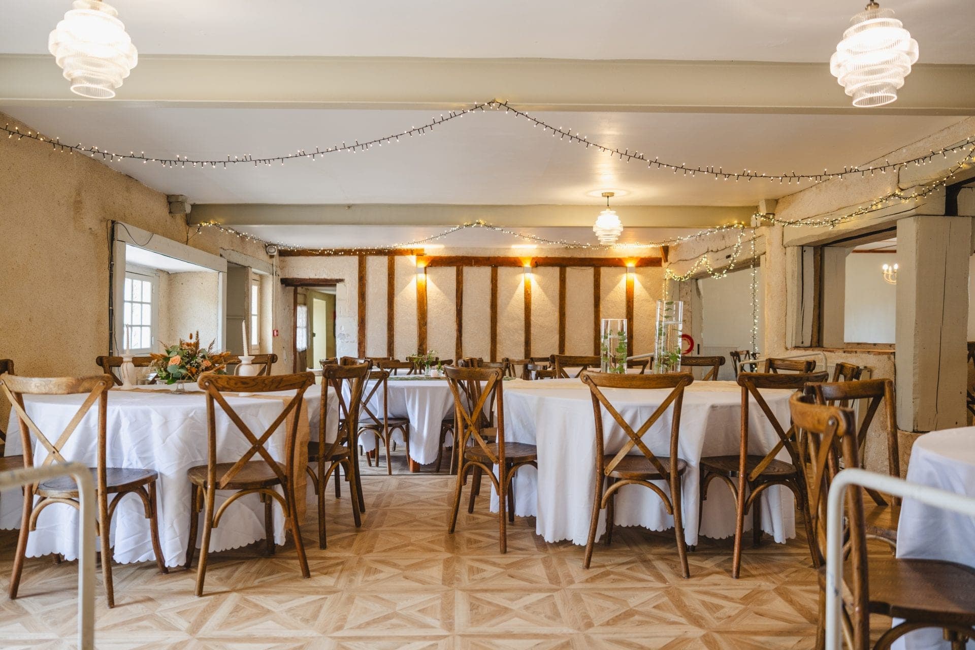 A reception room with round tables set for a wedding, decorated with fairy lights.
