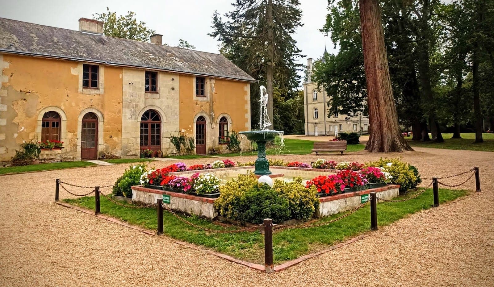 A fountain surrounded by flowerbeds in the grounds of a chateau.