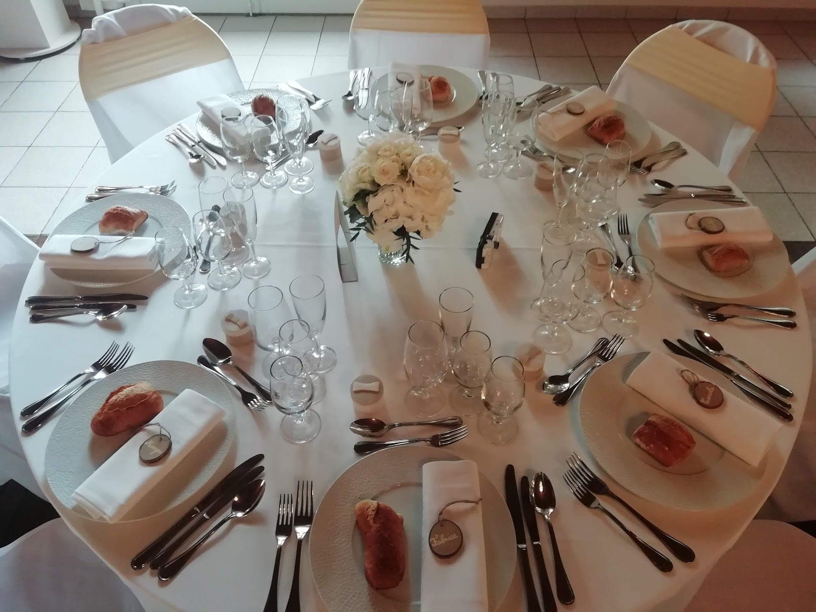 A round table set for a wedding reception with white linens and floral centerpieces.