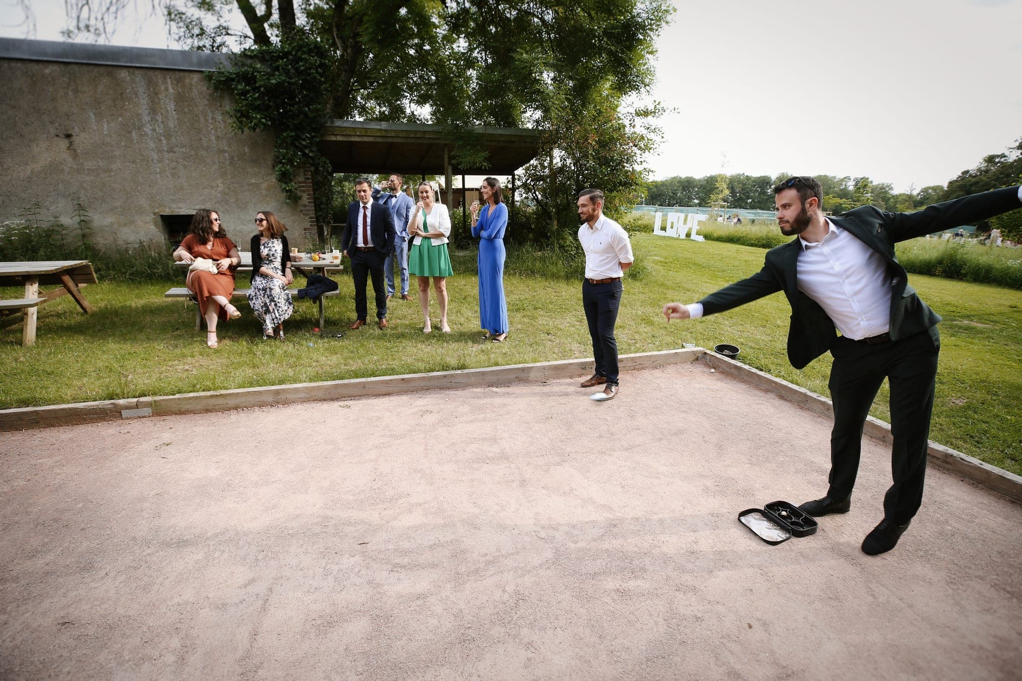 Guests play bocce ball on a court at a wedding venue with a large LOVE sign in the background.