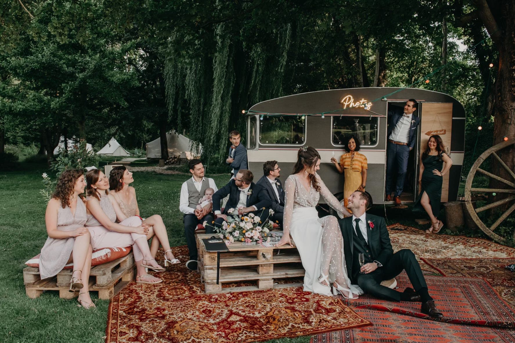 Wedding guests and a caravan in a grassy outdoor setting.
