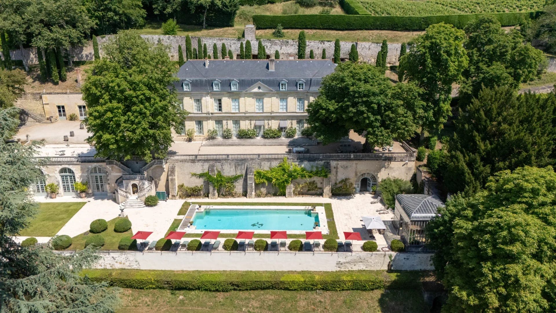 Aerial view of a French chateau with a swimming pool and gardens.