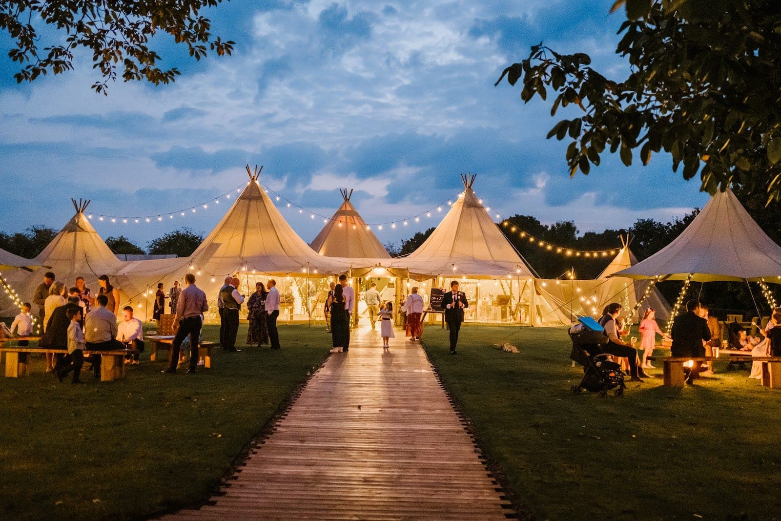 Tipis and string lights at a wedding reception with guests on the lawn.