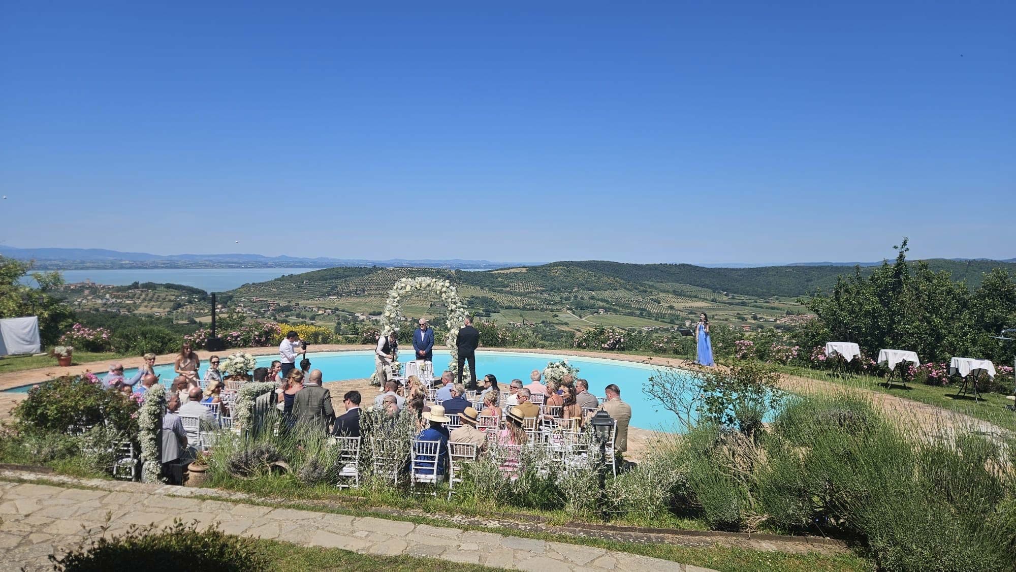Wedding ceremony by a pool with guests seated and a floral arch.