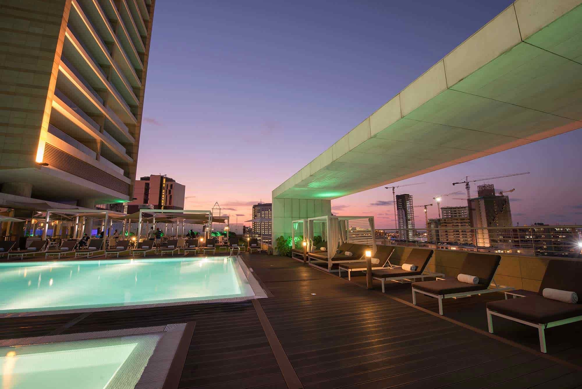 Rooftop pool area with lounge chairs and city view at dusk.