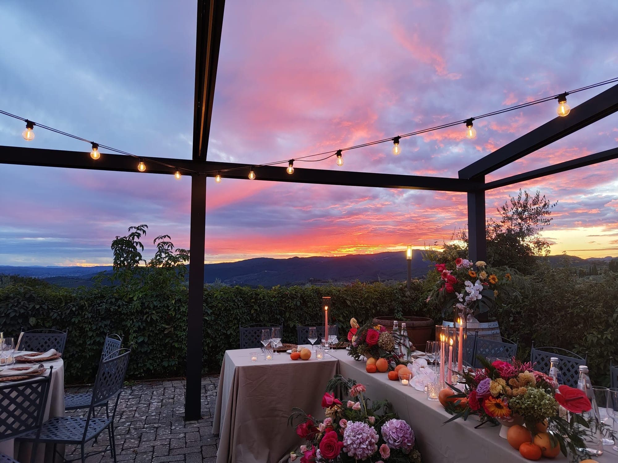 A reception table set for dinner on a terrace overlooking hills at sunset.