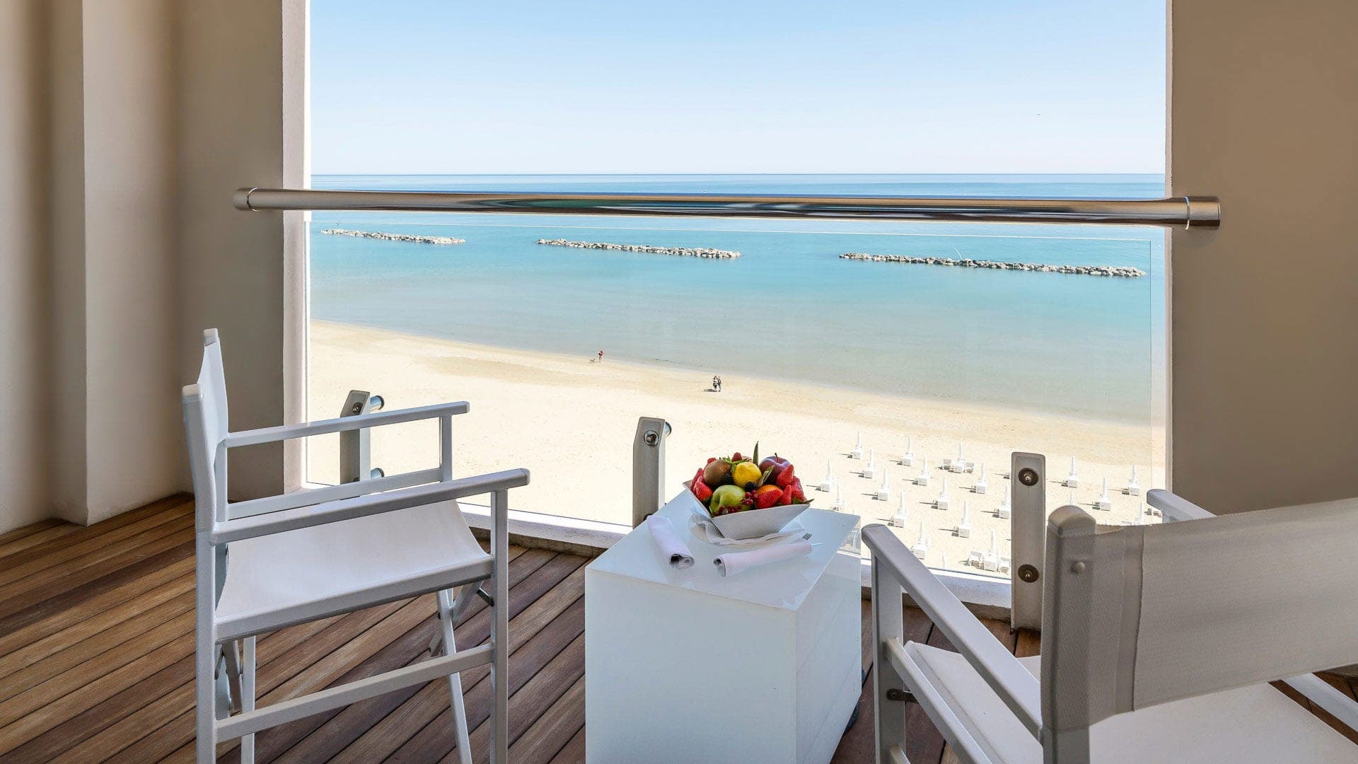 Balcony with chairs and a table overlooking a sandy beach and the sea.