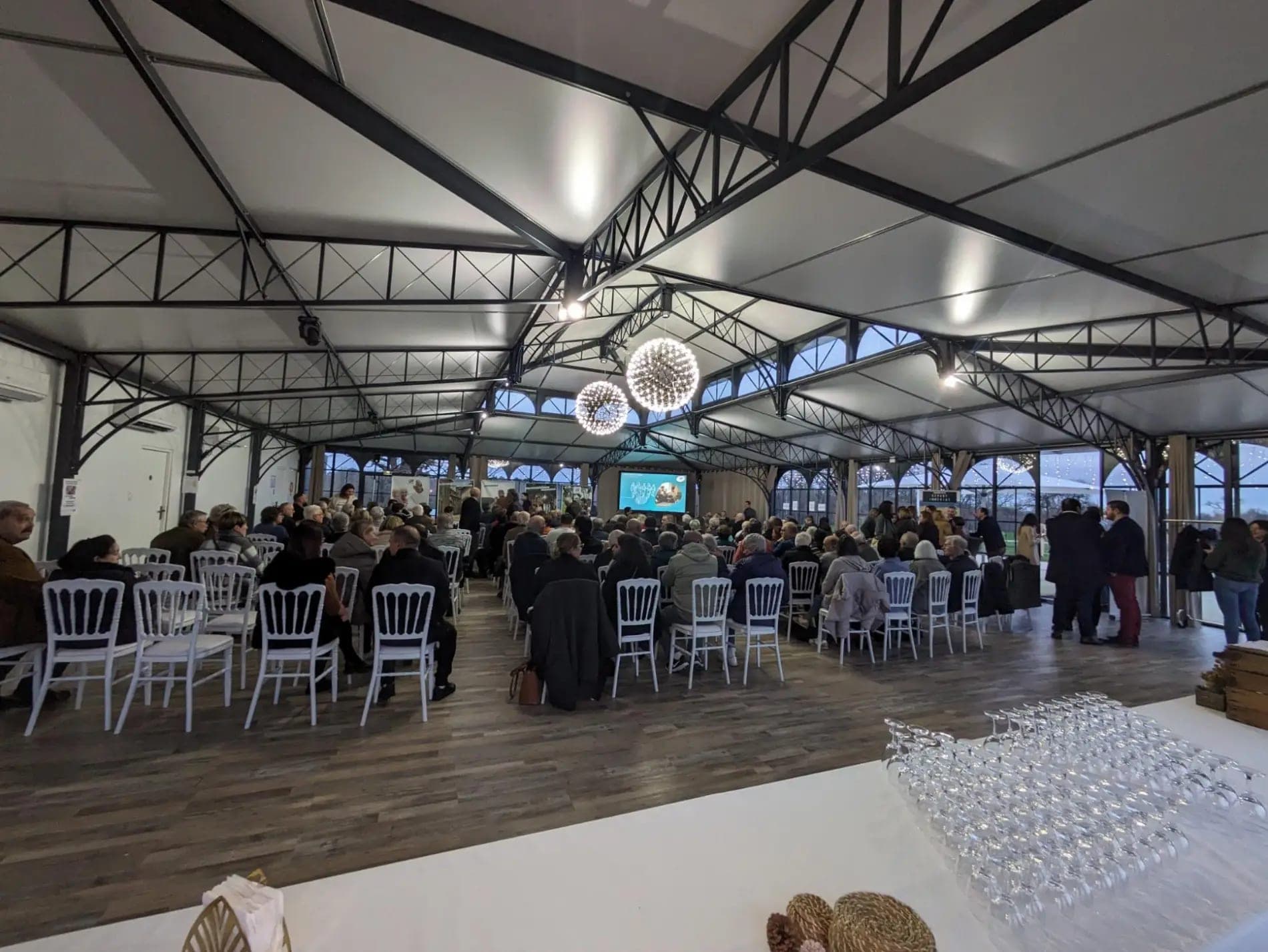Indoor event space with rows of chairs and tables, and a screen at the front.