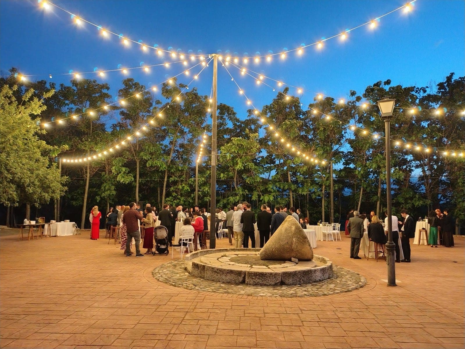 Evening wedding reception with guests and string lights outdoors.