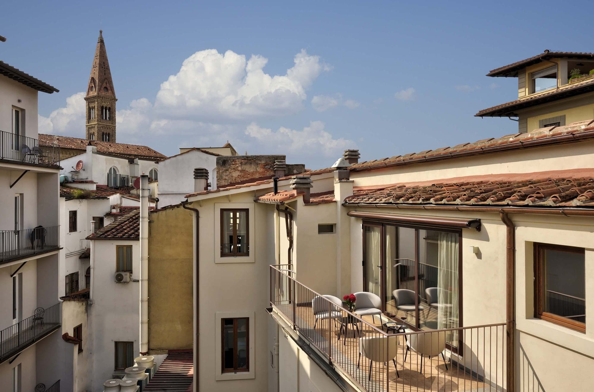 Balcony with chairs and tables overlooking Florentine rooftops and a bell tower.