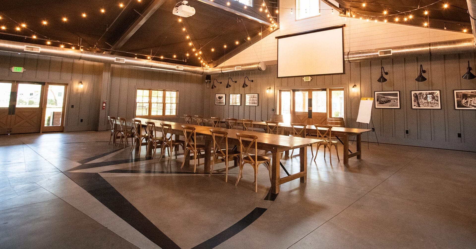 Indoor event space with long wooden tables and chairs, decorated with string lights.