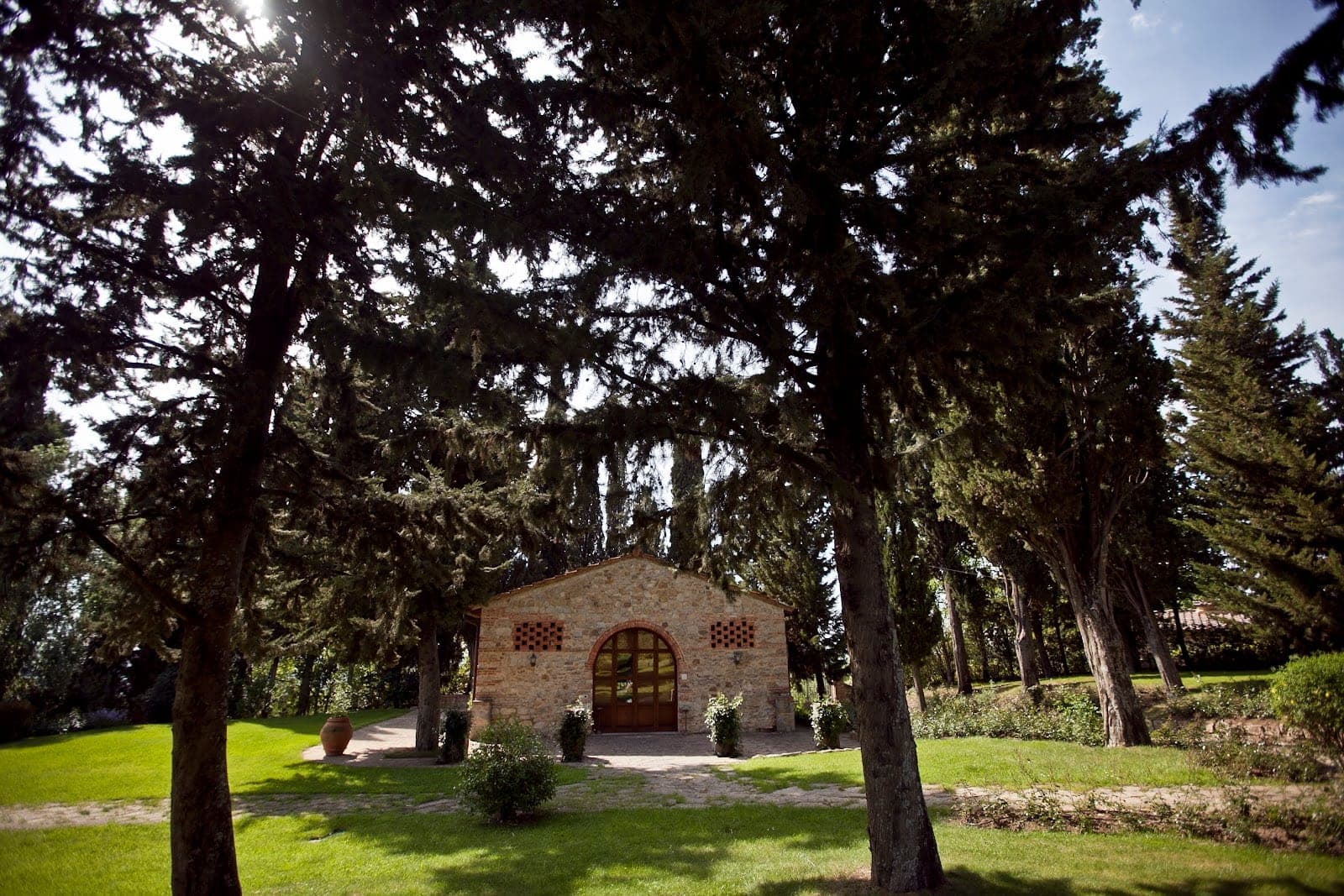 Stone building with arched doorway in a garden with trees.