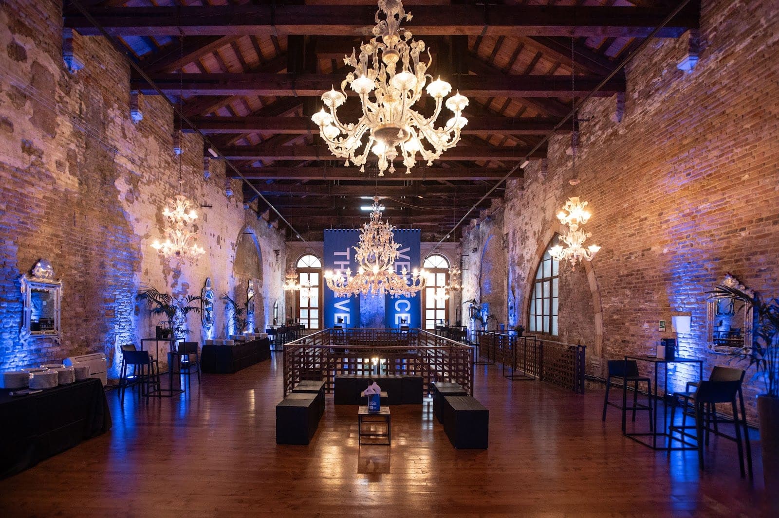 A large hall with brick walls, chandeliers, and catering stations.