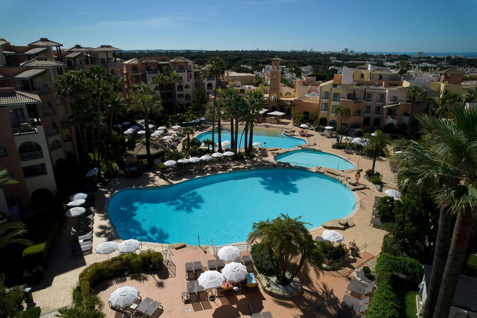 Resort with swimming pools and palm trees under a blue sky.
