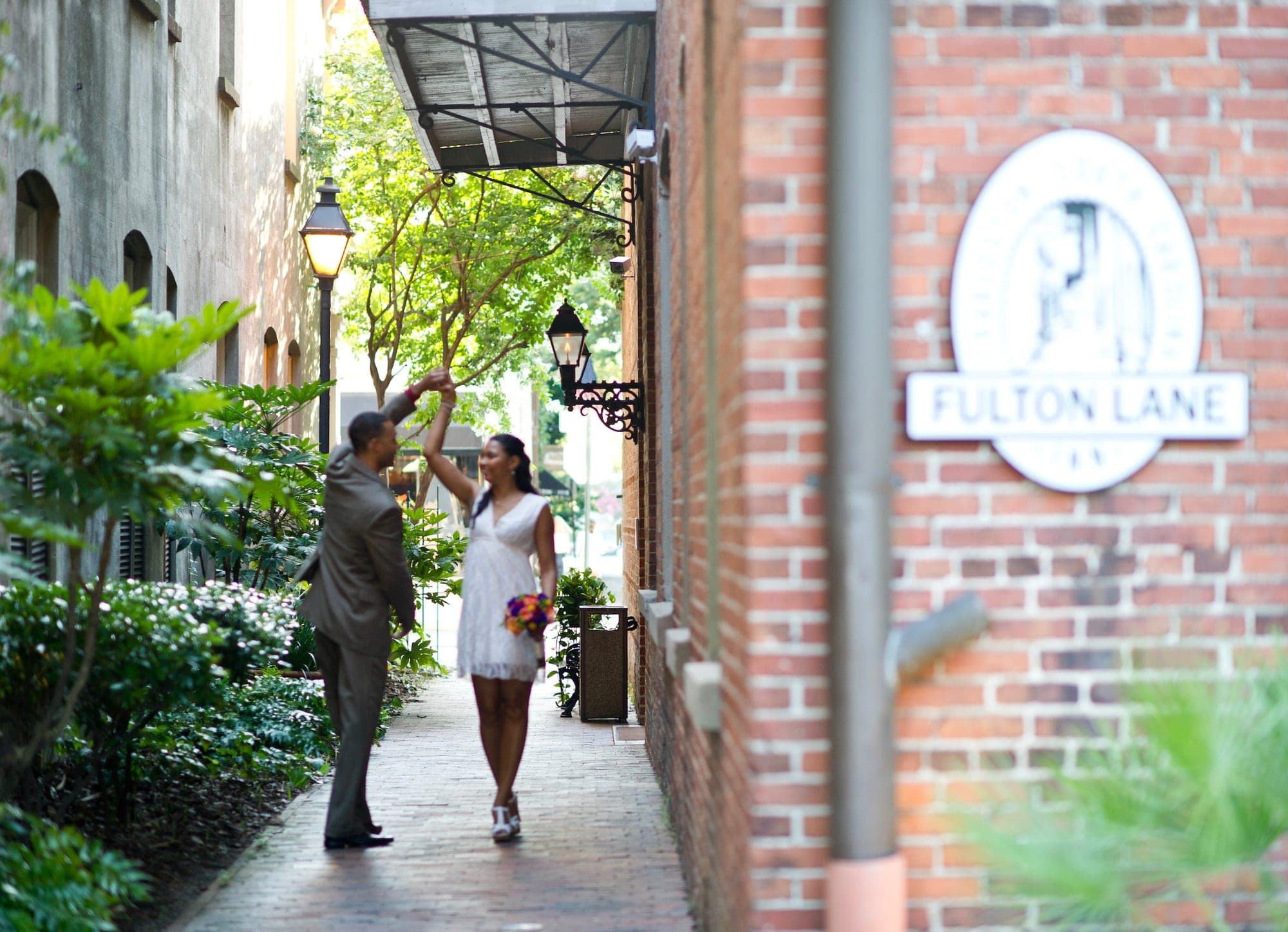 A couple dances in a brick alleyway with a sign that reads Fulton Lane.