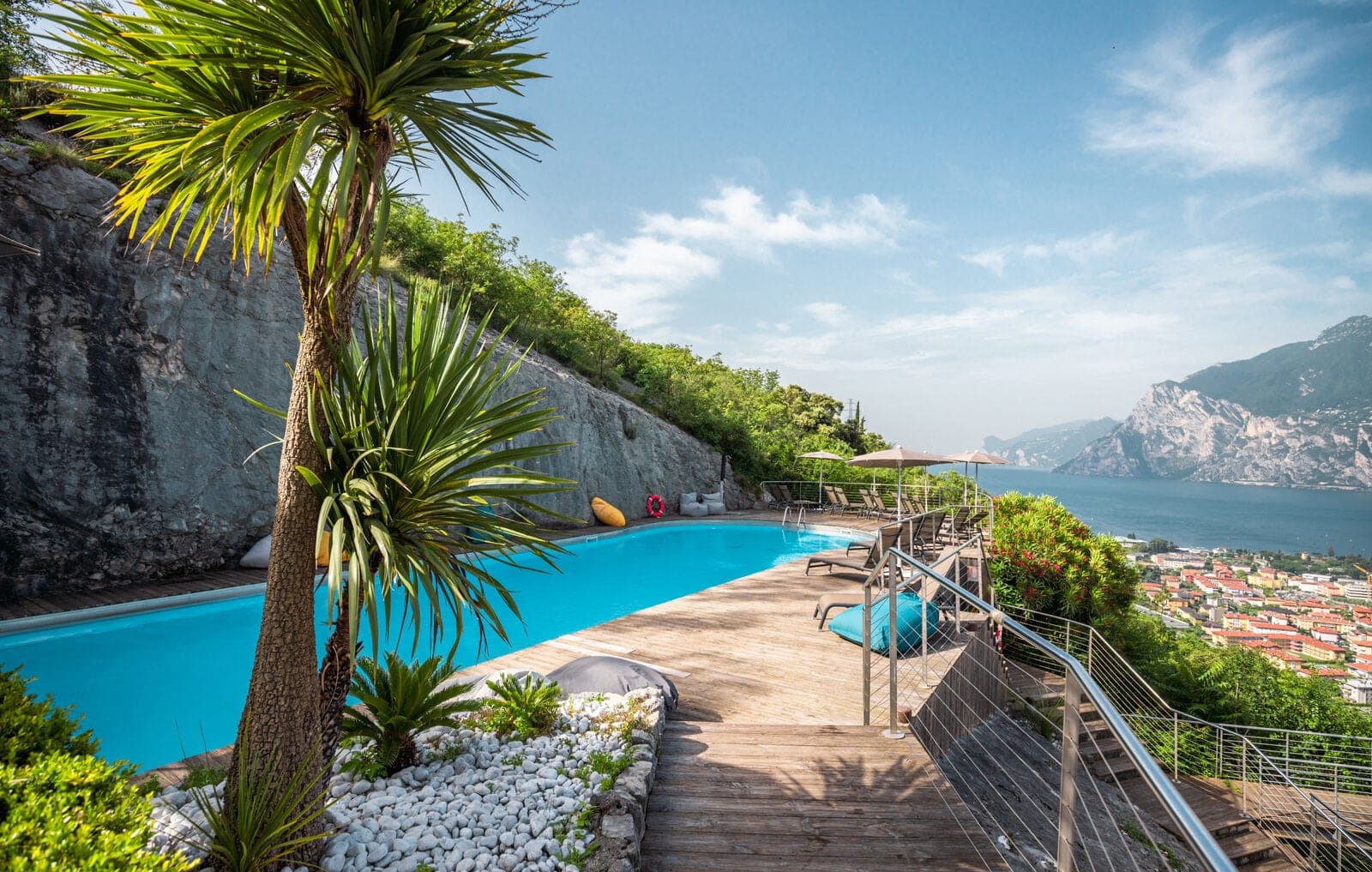 Swimming pool with loungers and umbrellas overlooking a lake and town.