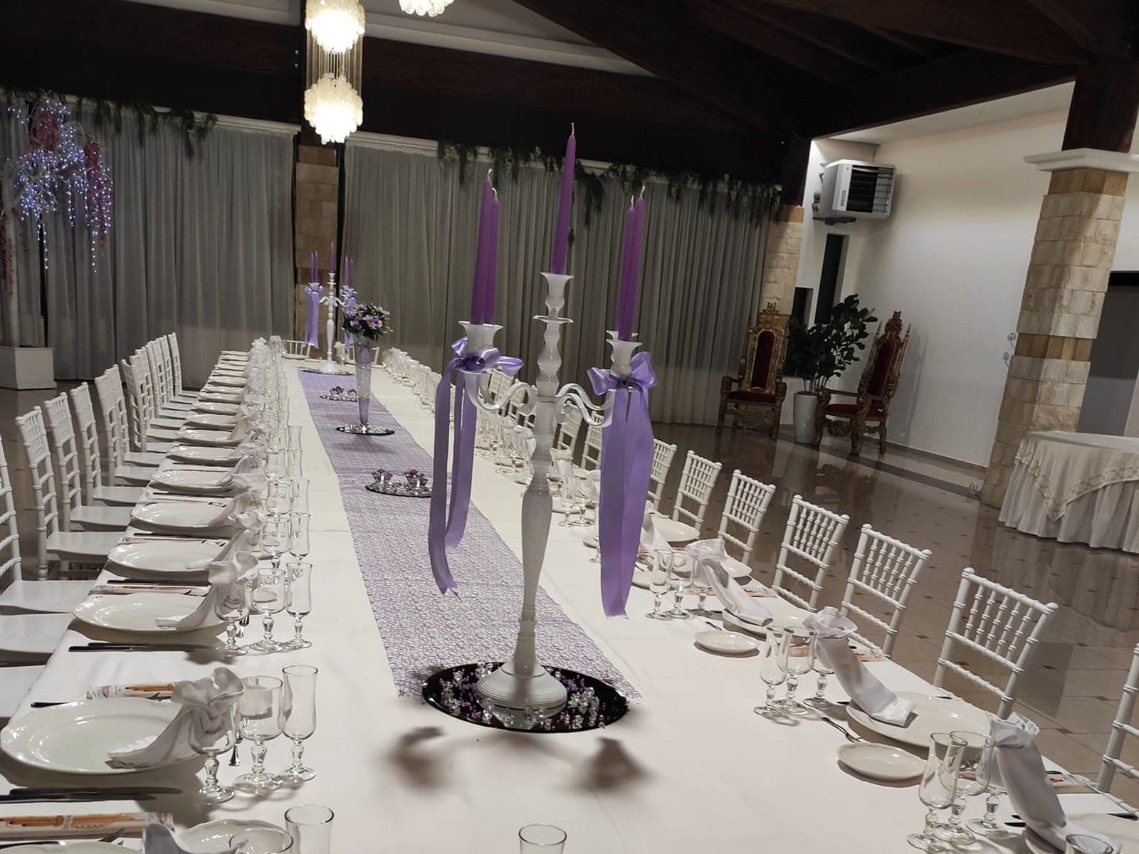 A long banquet table is set for a wedding reception with purple accents.
